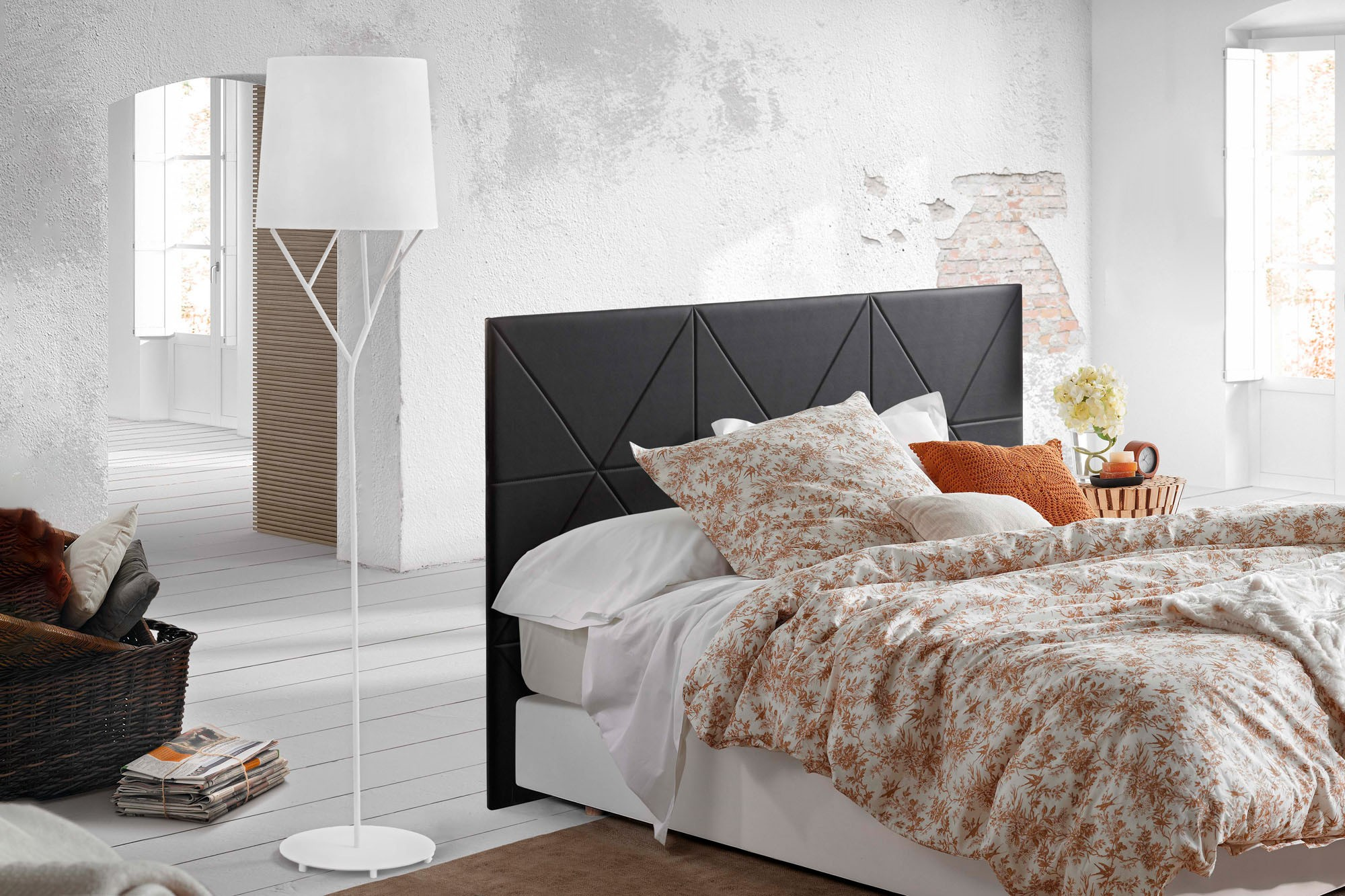 Una scena di camera da letto con un letto, una lampada e una finestra. Il muro è bianco e usurato.