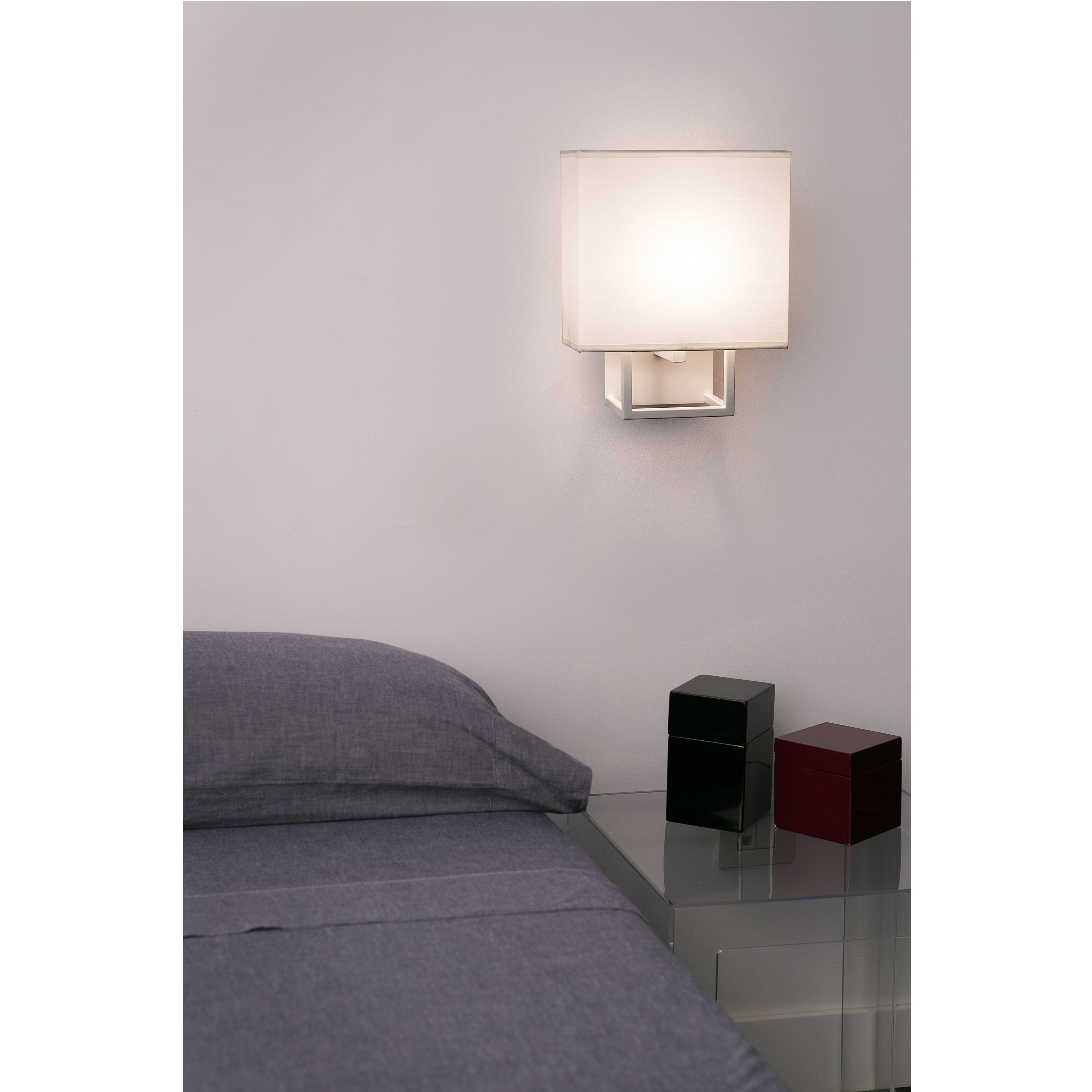 Scena di camera da letto con lampada a parete e letto. Comodino in vetro con due scatole.