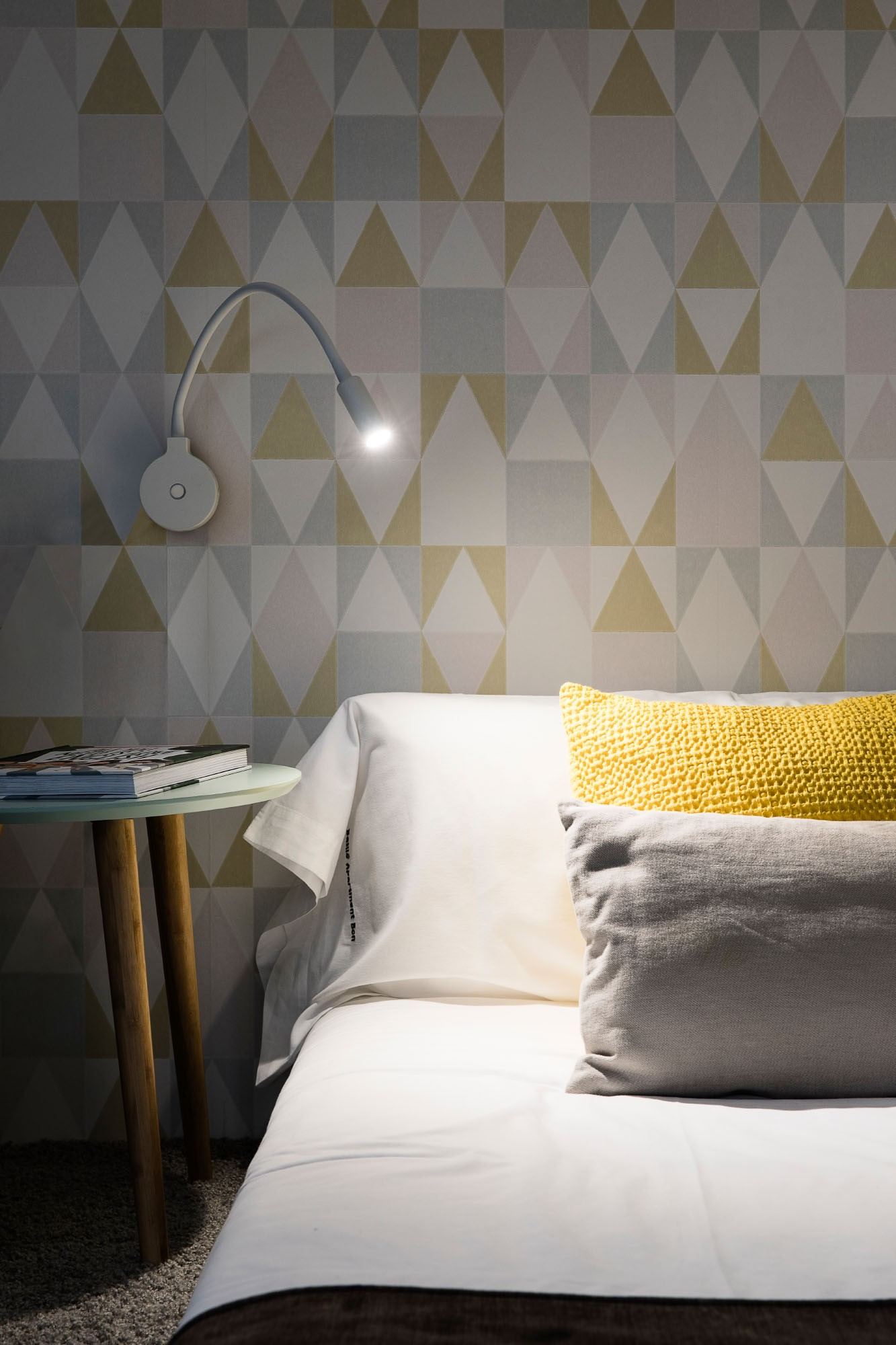 Una scena della camera da letto con letto, comodino, lampada e carta da parati a motivi.