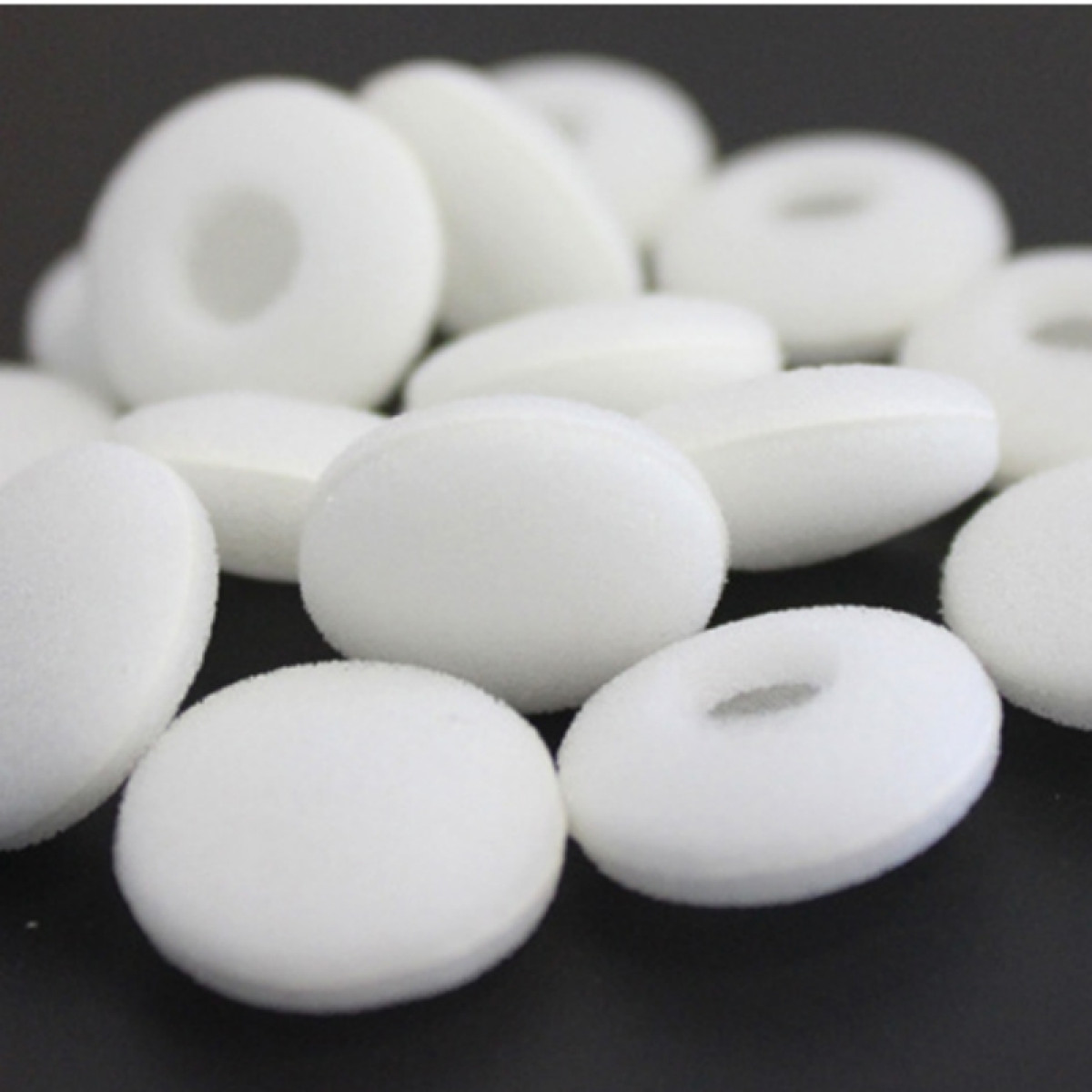 Białe gąbki do słuchawek, w kształcie obwarzanków, nieregularnie ułożone.