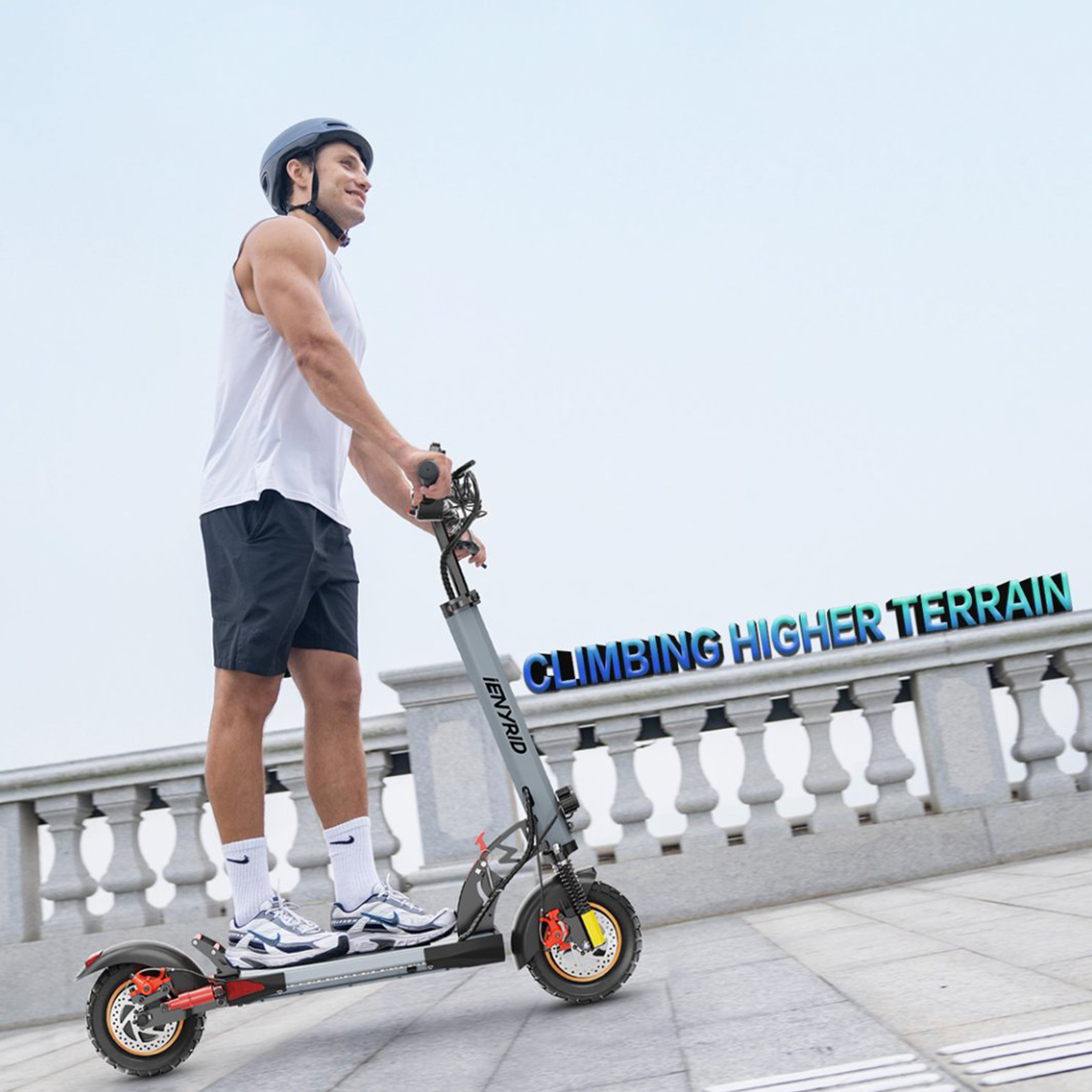 Mężczyzna jadący szarą hulajnogą elektryczną po utwardzonej ścieżce, ze słowami 'CLIMBING HIGHER TERRAIN'.