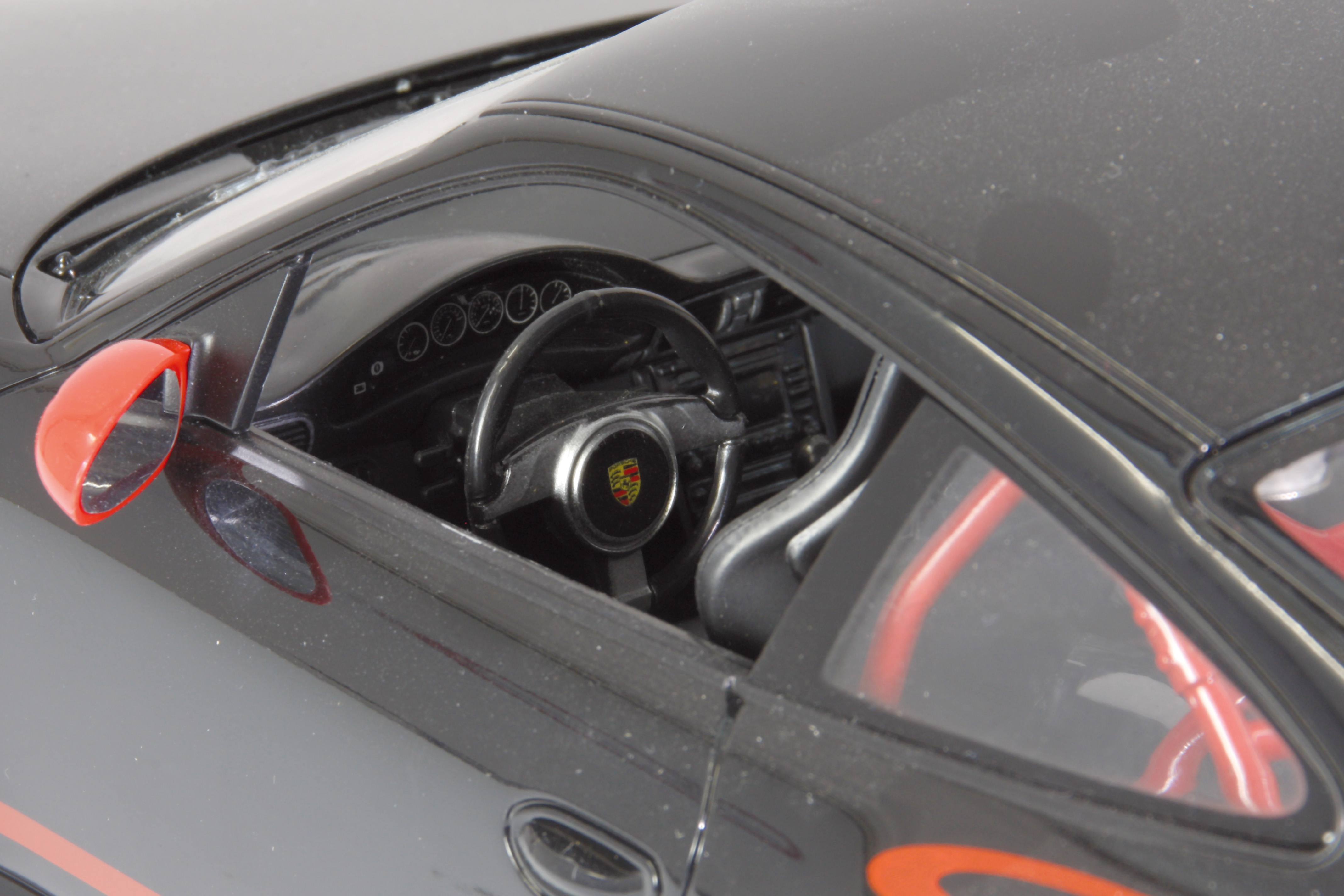 Czarne wnętrze samochodu z kierownicą i czerwonymi elementami.