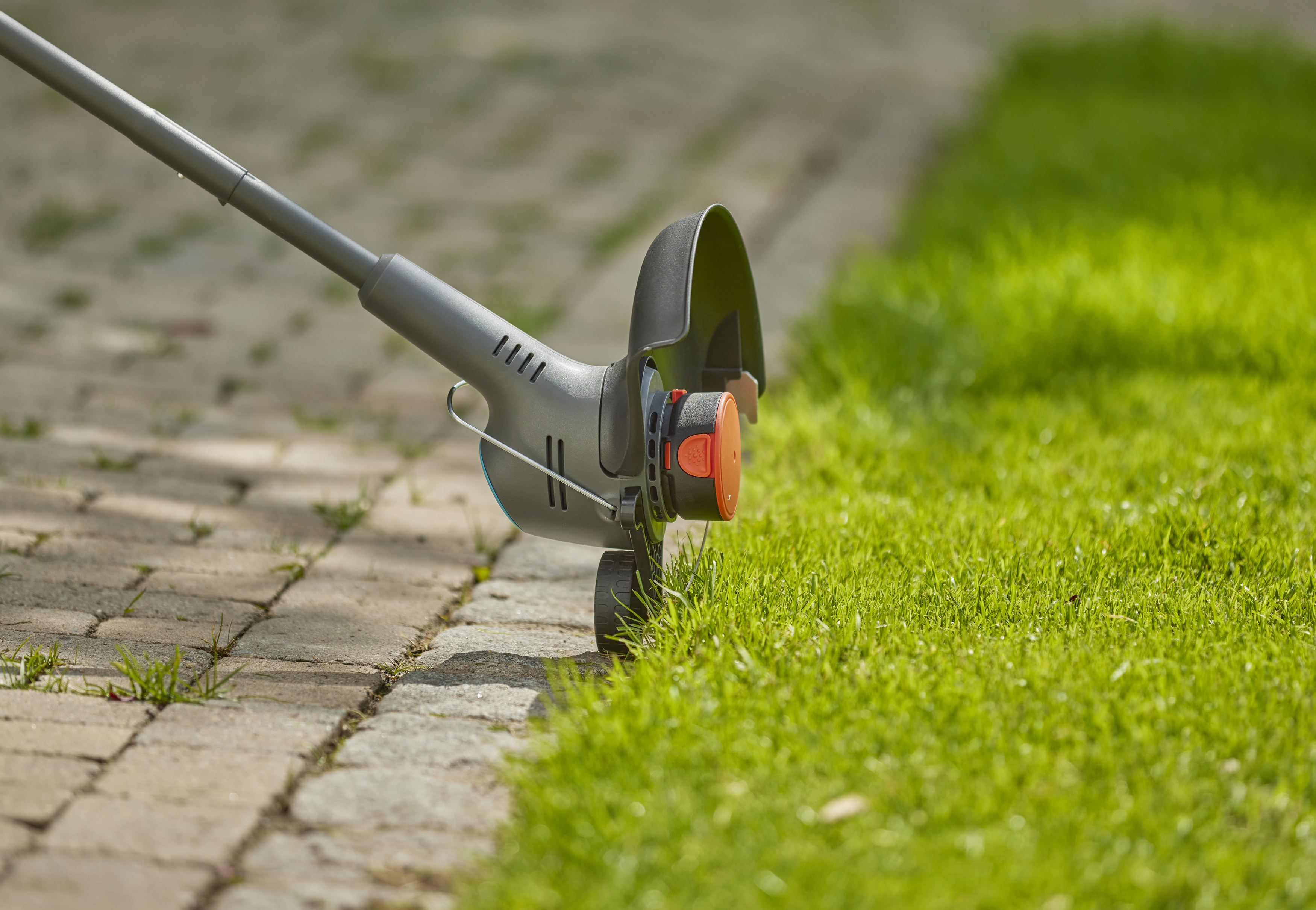 Ein Trimmer schneidet Gras entlang einer Backsteinkante.