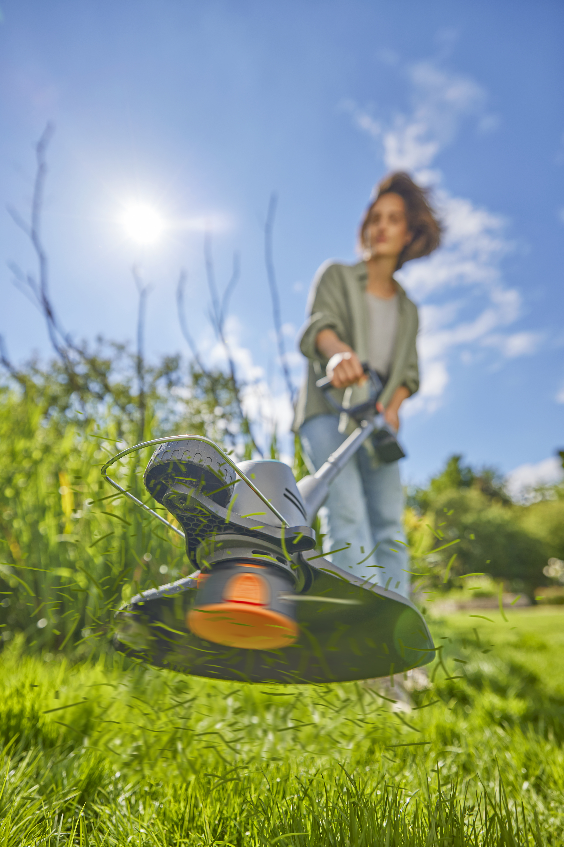 Person verwendet einen schwarzen und grauen Rasentrimmer, Gras fliegt in der Luft, blauer Himmel.