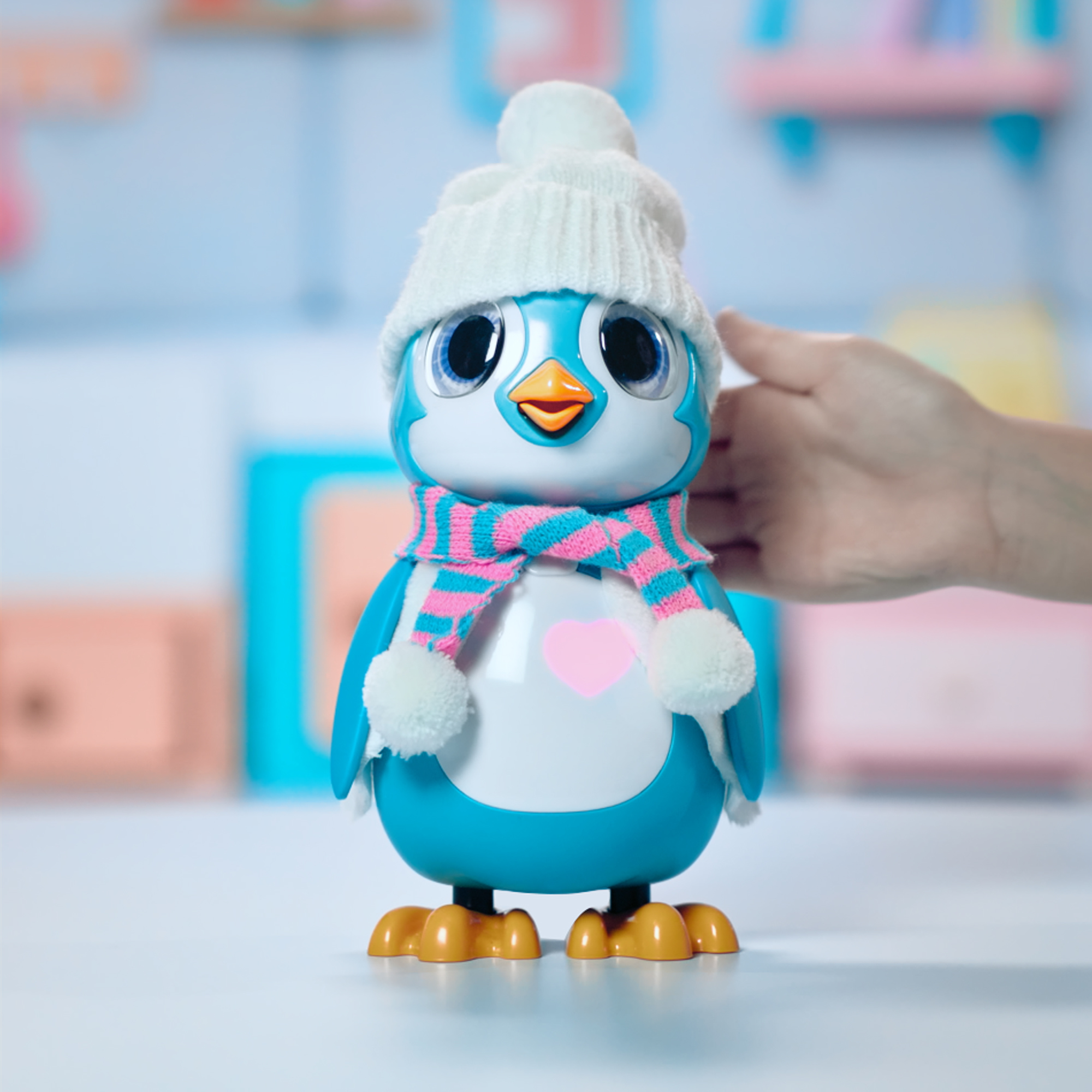 Un giocattolo a forma di pinguino con un cappello bianco e una sciarpa rosa e blu. Una persona lo sta toccando.