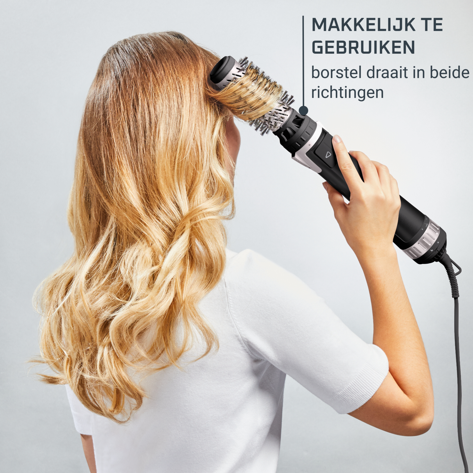 Una donna si acconcia i capelli con una spazzola per lo styling nera e argentata, vista da dietro.