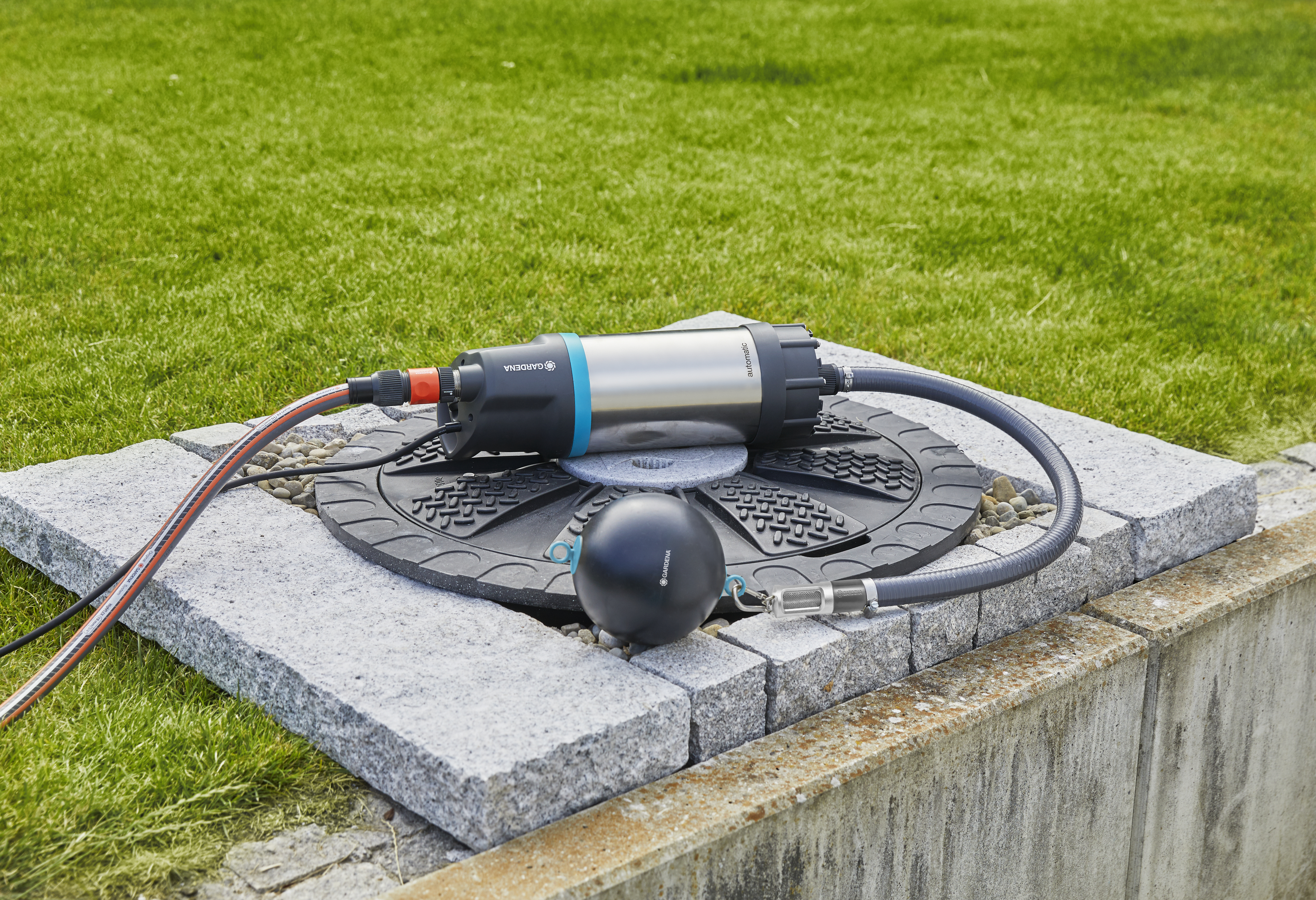 Pompa jest ustawiona w ogrodzie z zielonym trawnikiem. Czarna kula i wąż również znajdują się na zdjęciu.