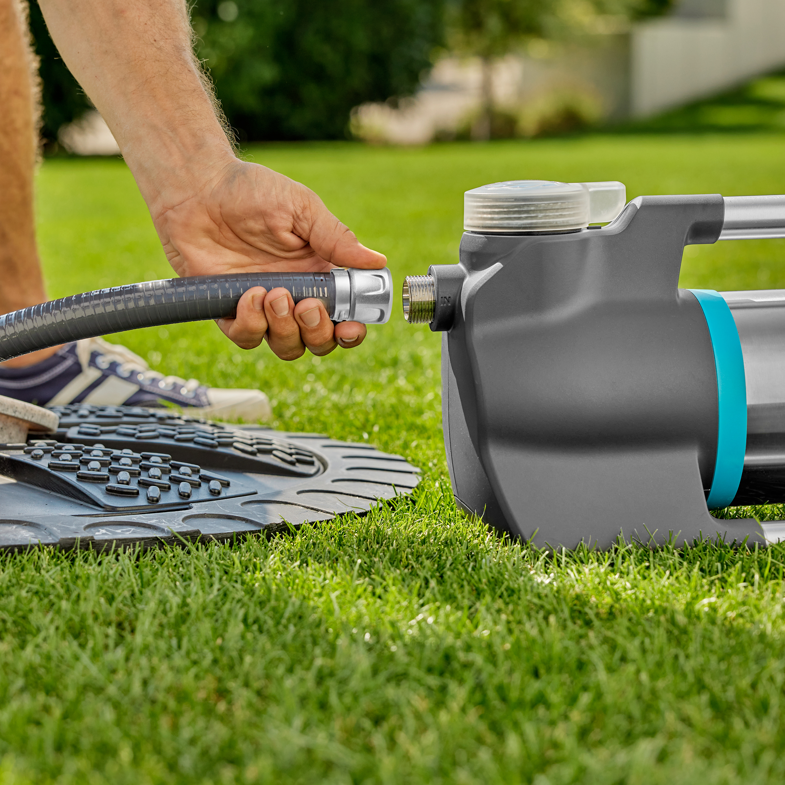 Osoba podłączająca szary wąż do szarej i turkusowej pompy wodnej na zielonej trawie.