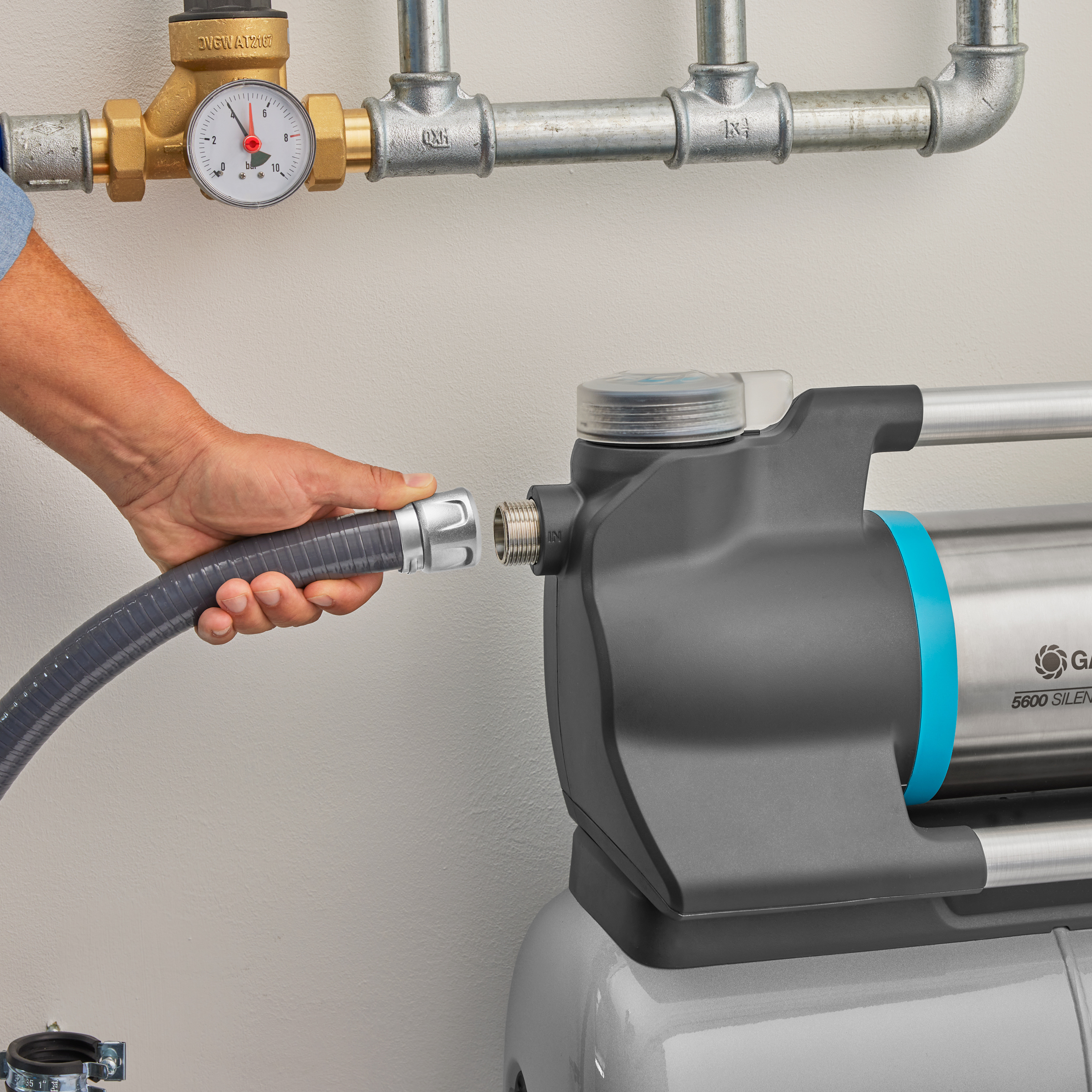 Osoba podłączająca szary wąż do pompy wodnej w pobliżu rur na ścianie.