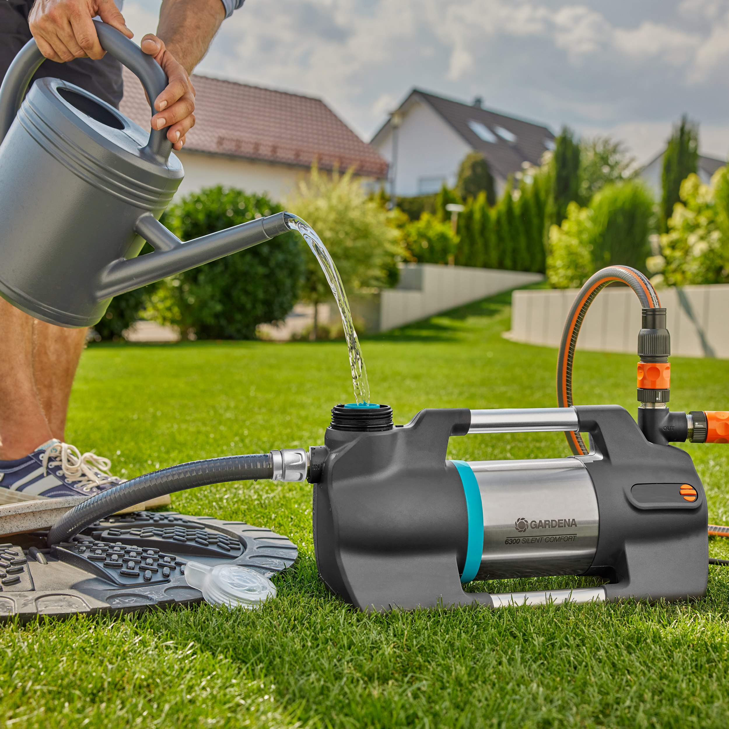 Mężczyzna podlewający pompę konewką. Zielona trawa, domy w tle.