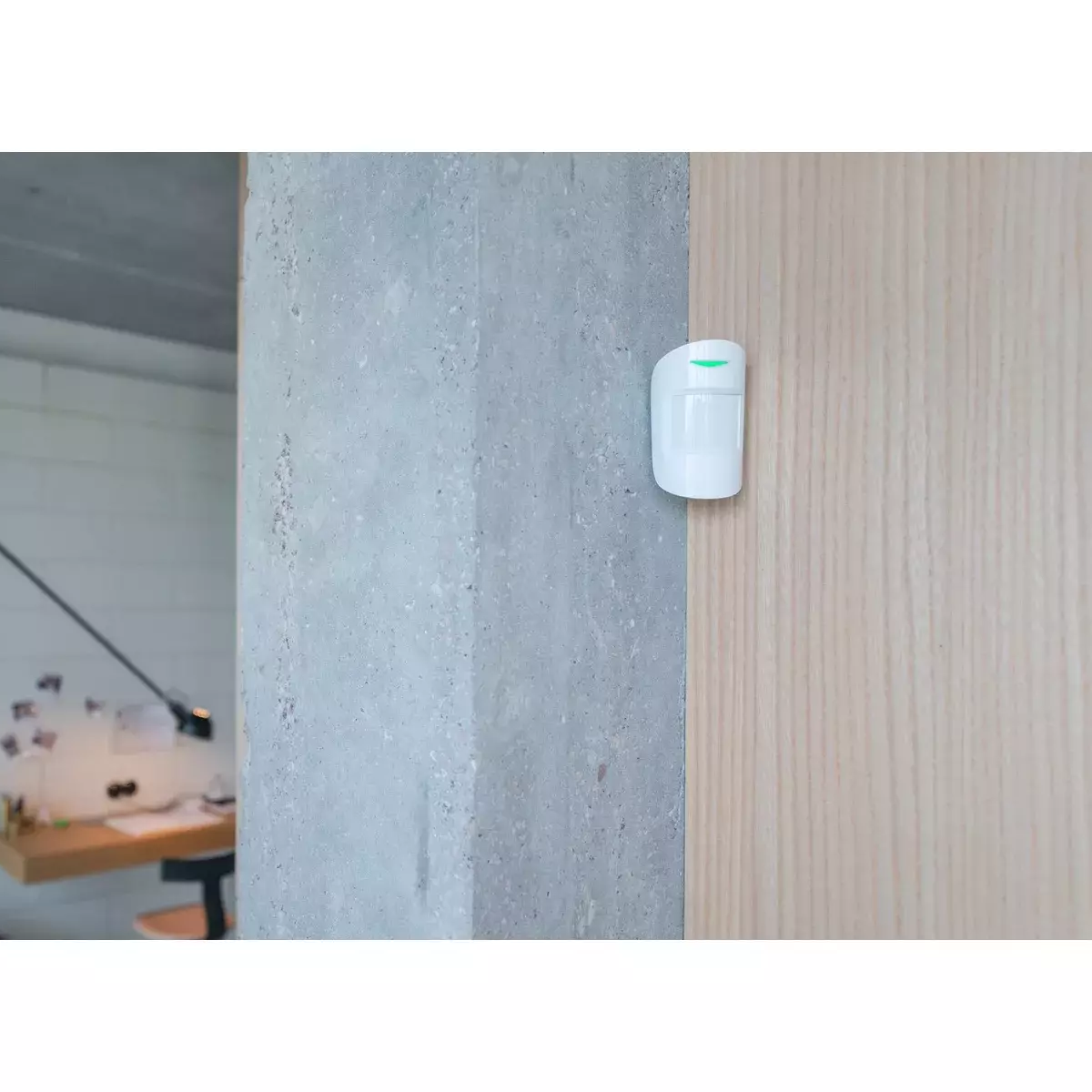 Sensor Ajax blanco montado en una pared gris. En una pared de madera. En una habitación.