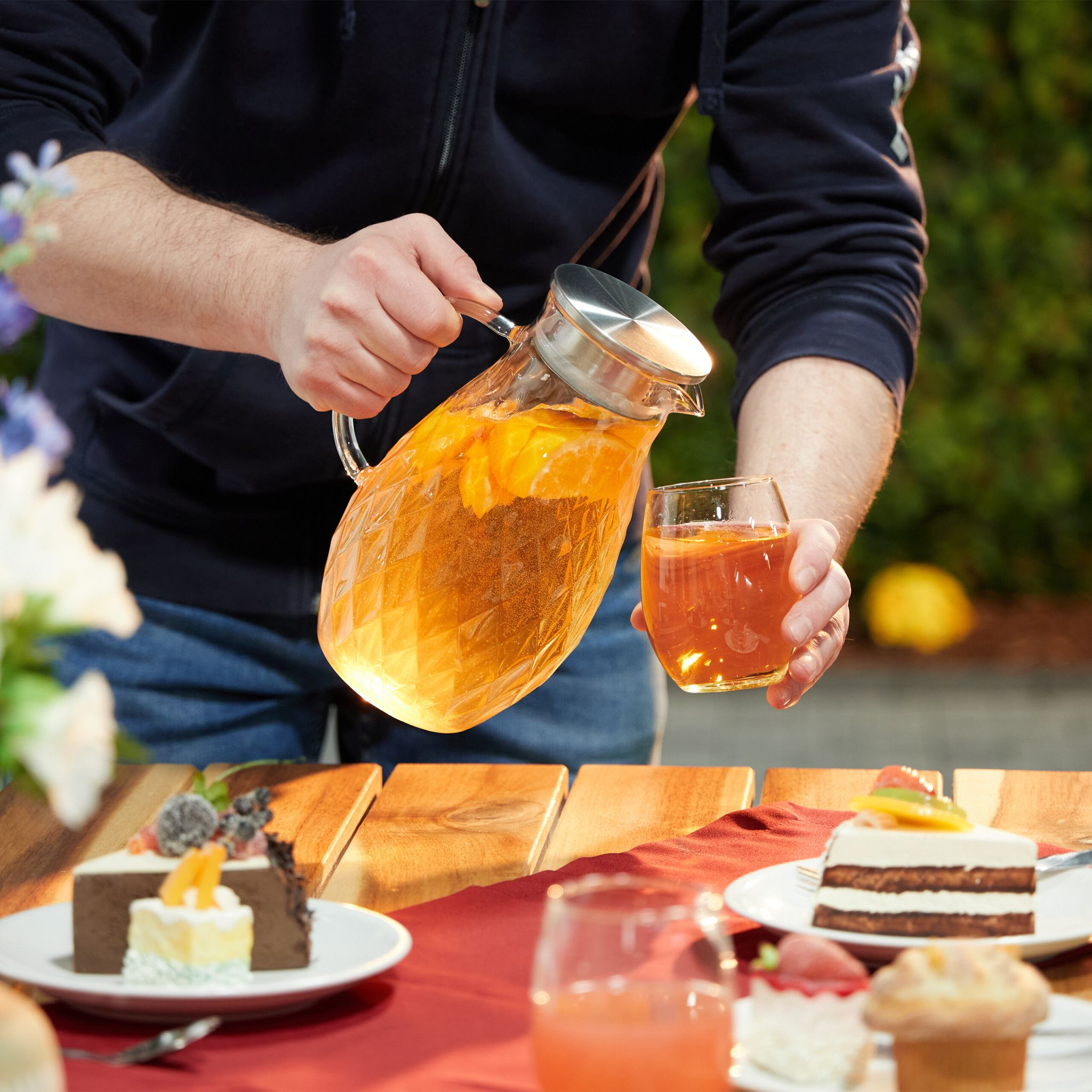 Person gießt Orangensaft aus einem Krug in ein Glas. Essen auf einem Tisch.