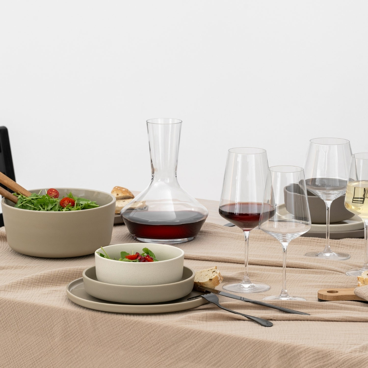 Table avec salade, verres à vin, carafe et assiettes. Nappe beige, fond blanc.