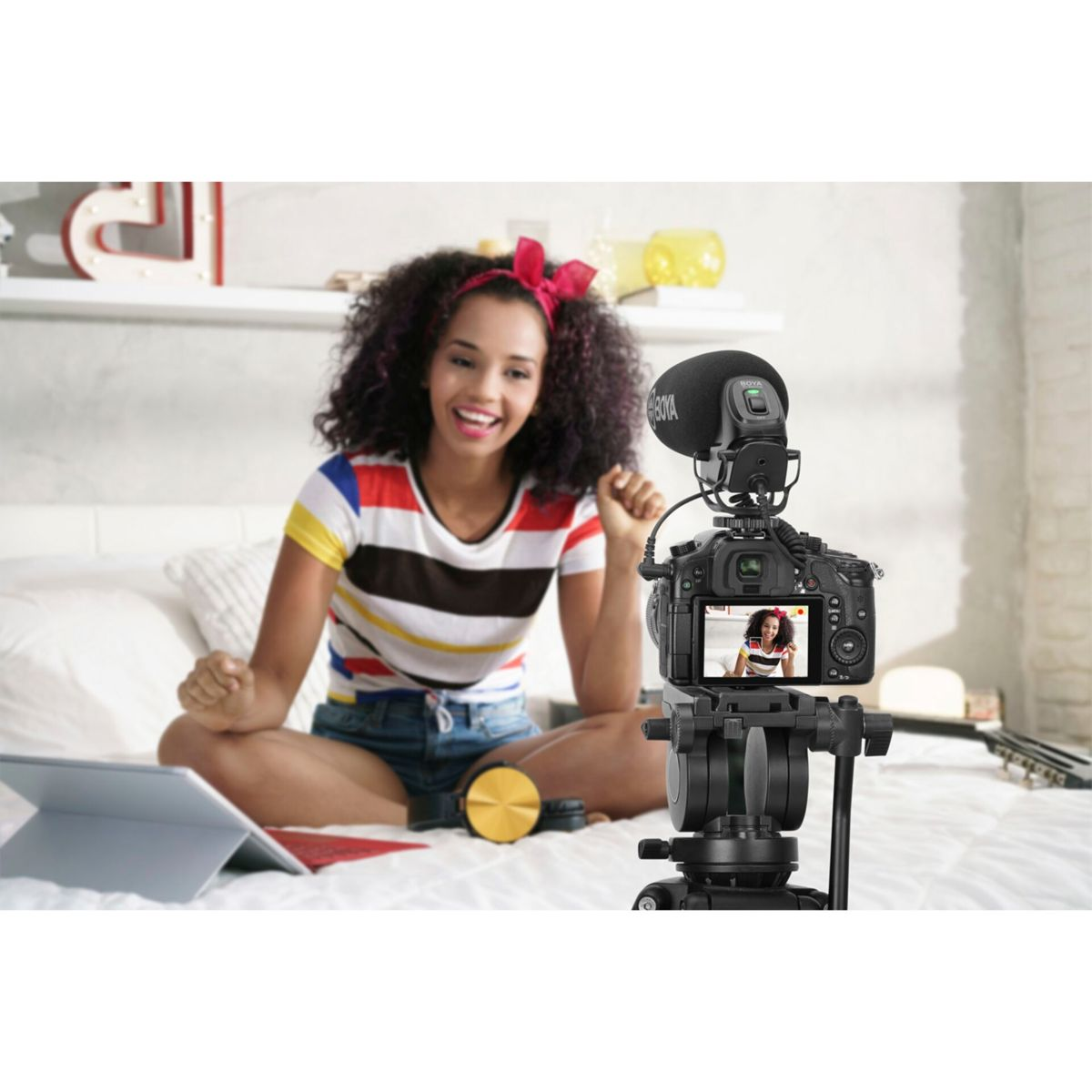 Kobieta nagrywa vloga za pomocą kamery i mikrofonu. Kamera pokazuje ją na ekranie.