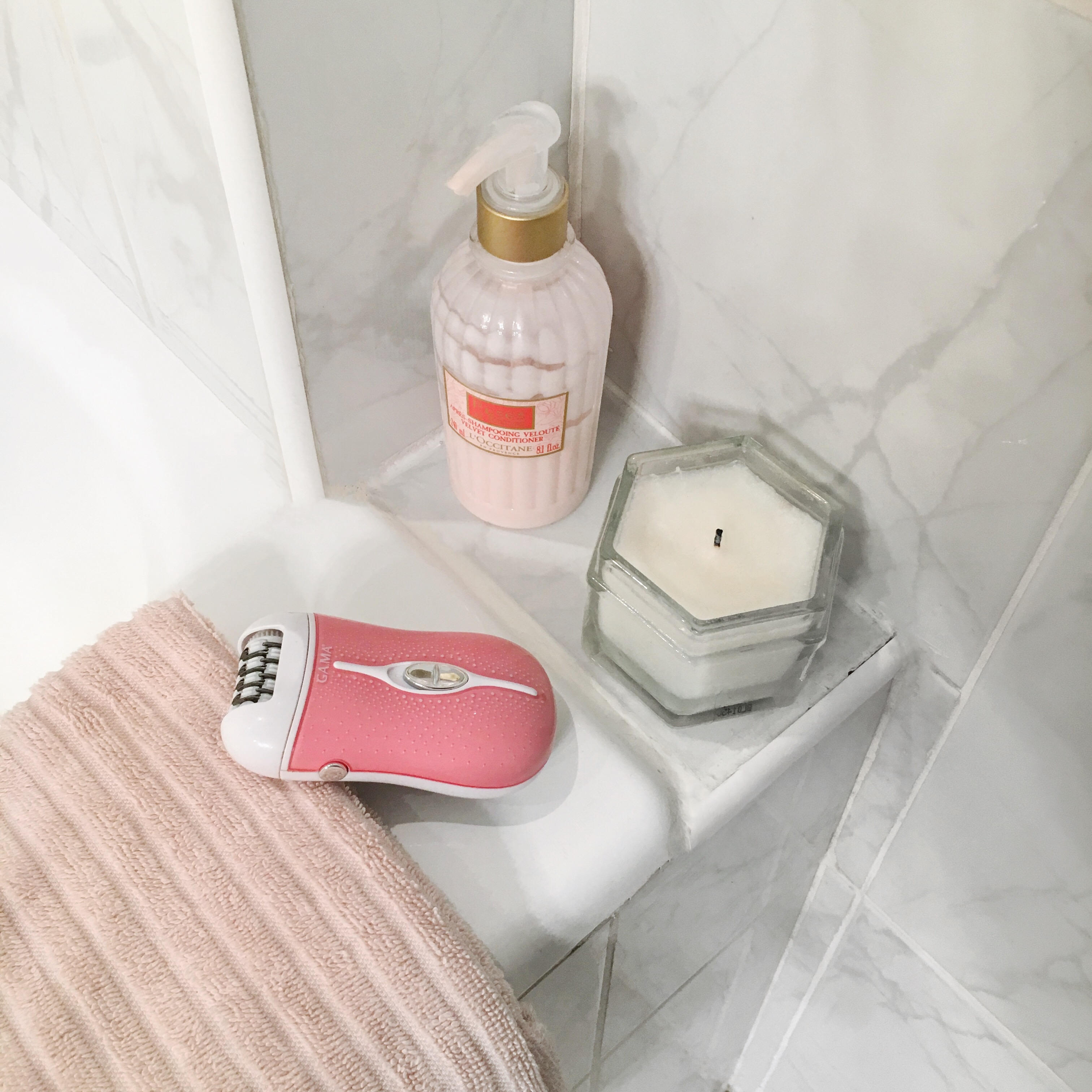 Rosa Epilierer auf einer Theke in der Nähe einer Kerze und Lotion. Rosa Handtuch daneben.