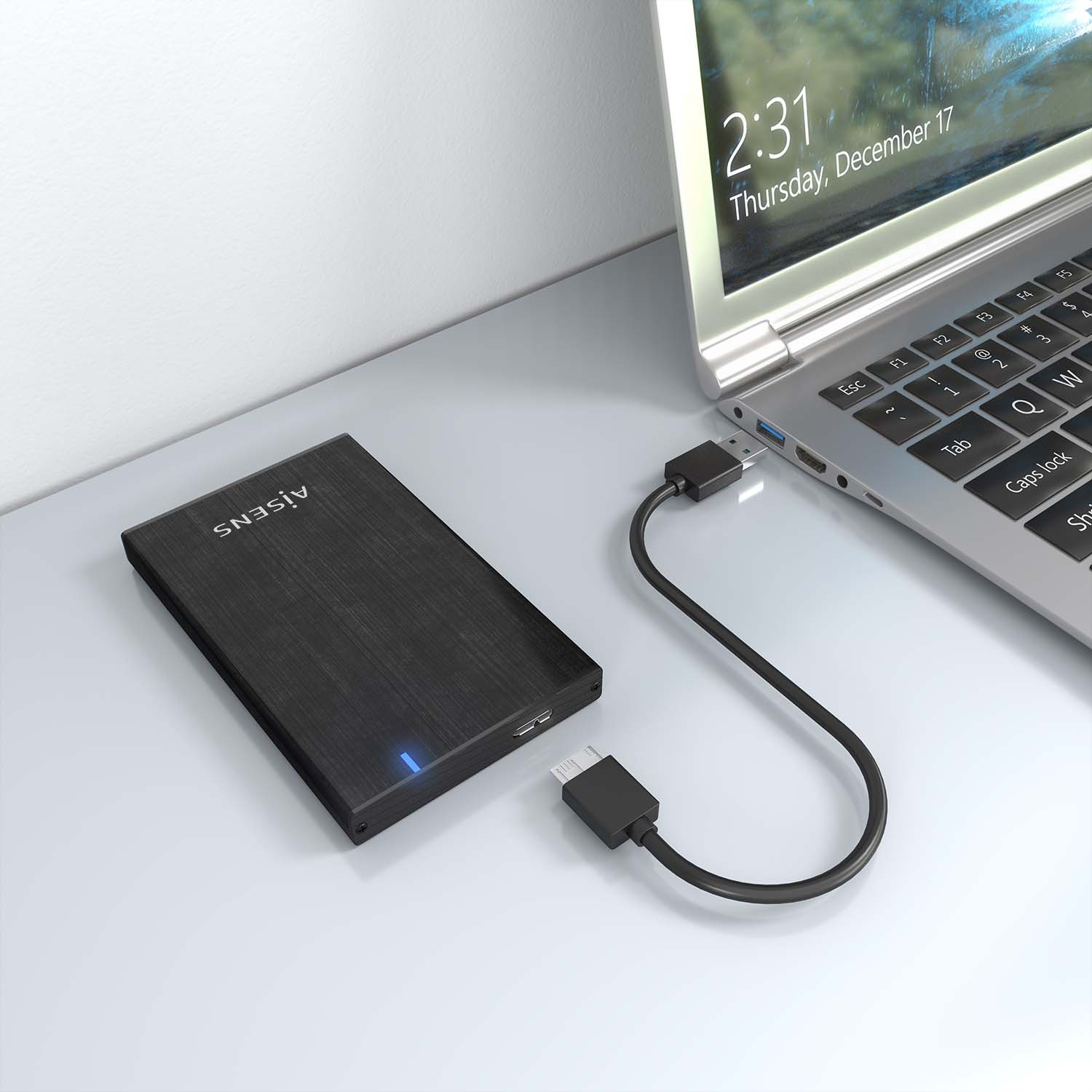 Disco rigido esterno nero collegato a un laptop. Cavo USB. Superficie bianca con luce blu.