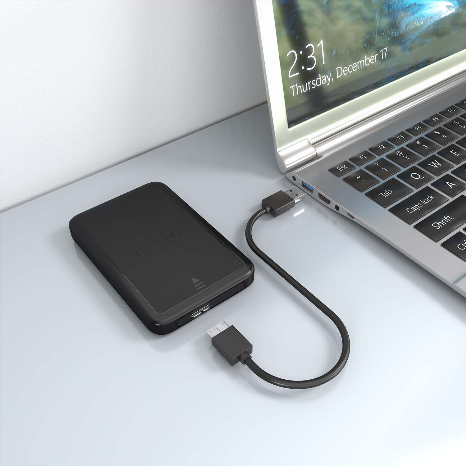 Disco rigido esterno nero con cavo collegato a un laptop, su una scrivania.