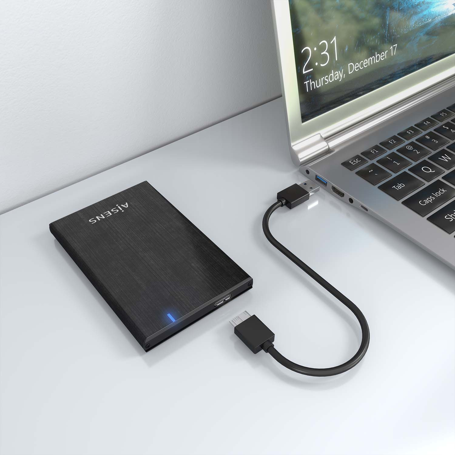 Disco rigido esterno nero, accanto a un laptop. Il cavo USB collega l'unità al laptop.