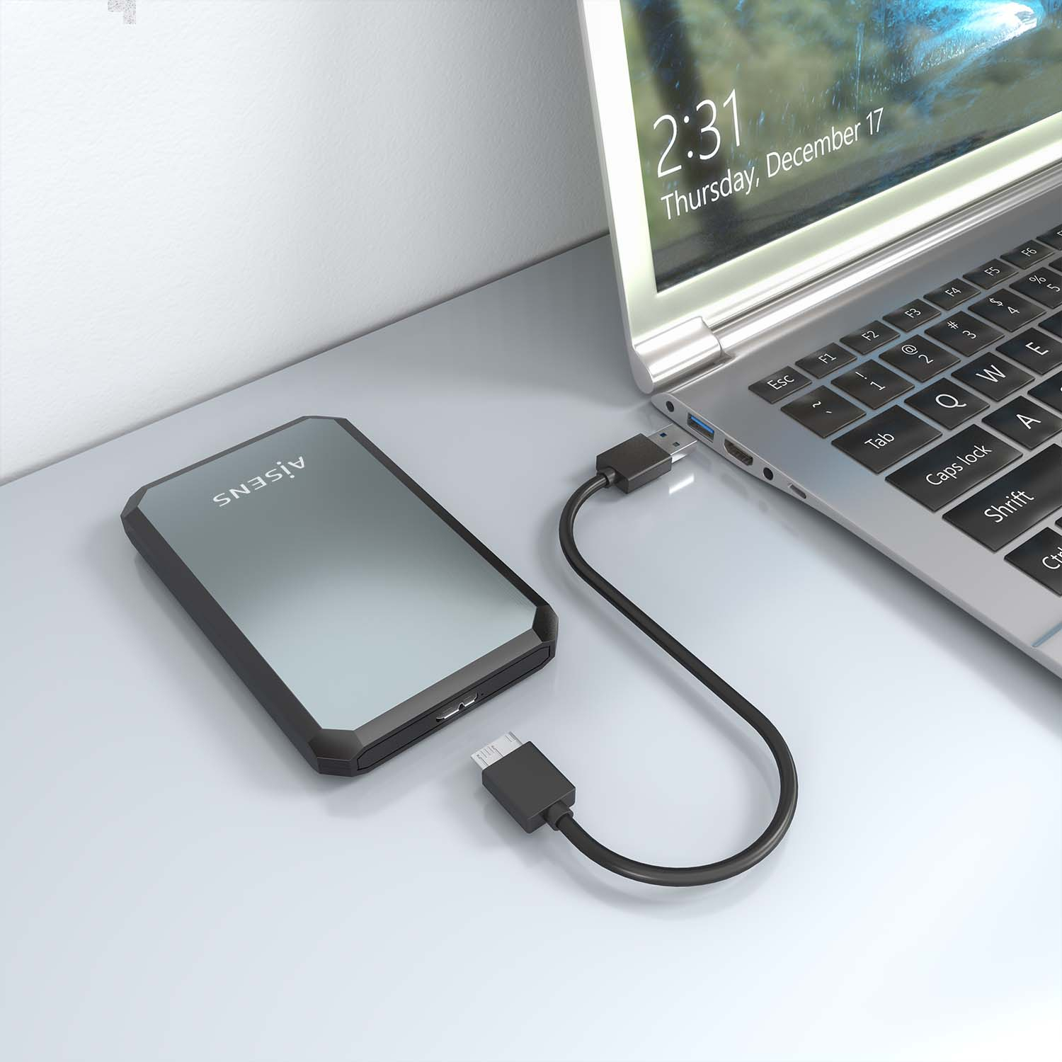 Disco rigido esterno collegato a un laptop tramite un cavo USB su una superficie chiara.