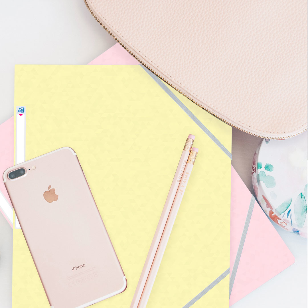 Układ płaski z artykułami papierniczymi, w tym telefonem, ołówkami, różowymi notatnikami i torebką.