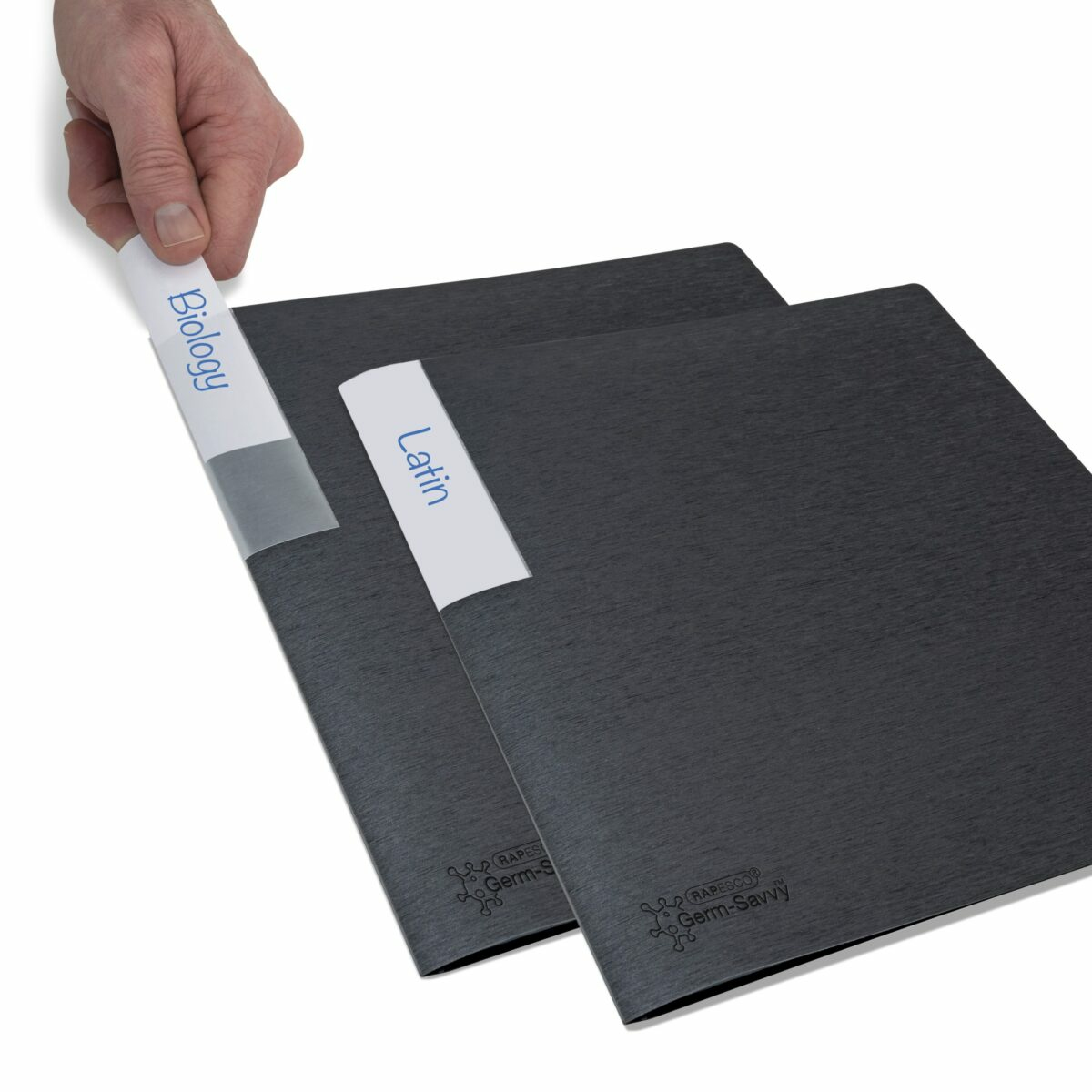 Ręka trzymająca etykietę 'Biologia' w czarnej teczce. Druga z napisem 'Łacina'. Tło: więcej teczek.