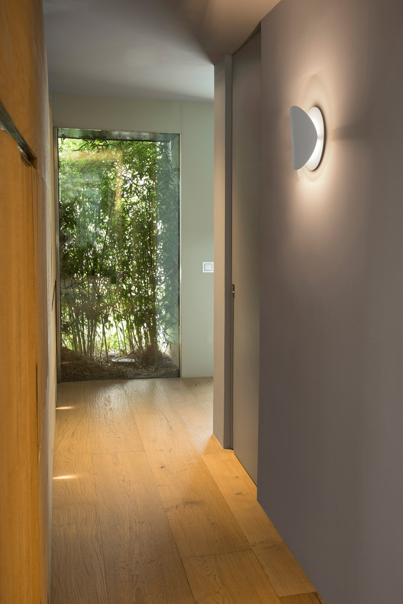 Corridoio con pavimento in legno, luce bianca moderna e finestra su uno spazio verde.
