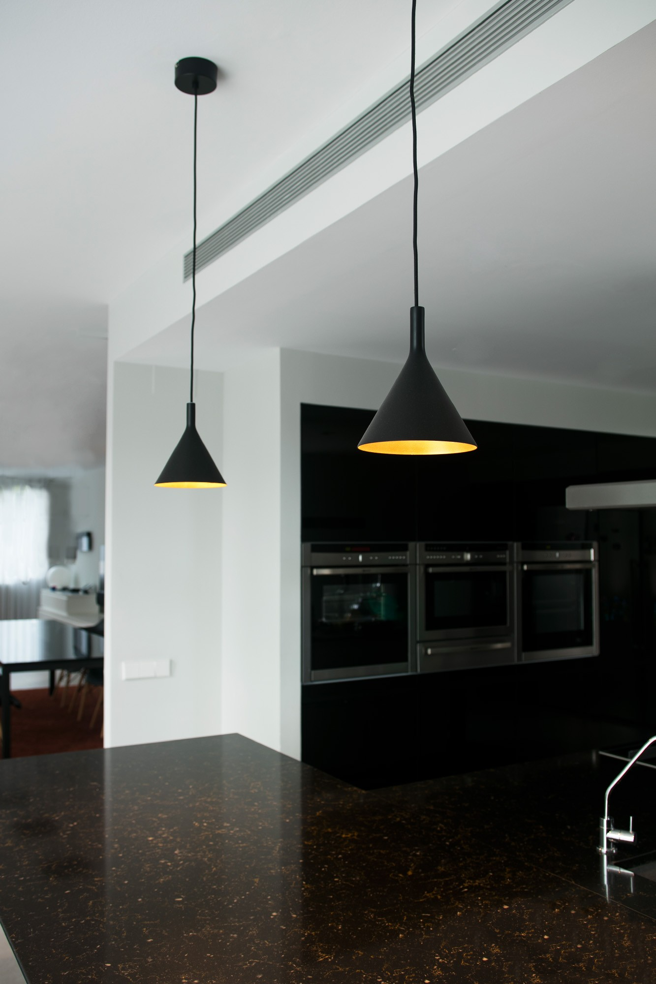 Due lampade a sospensione nere a forma di cono sono appese sopra un piano cucina. Le luci sono sospese al soffitto.