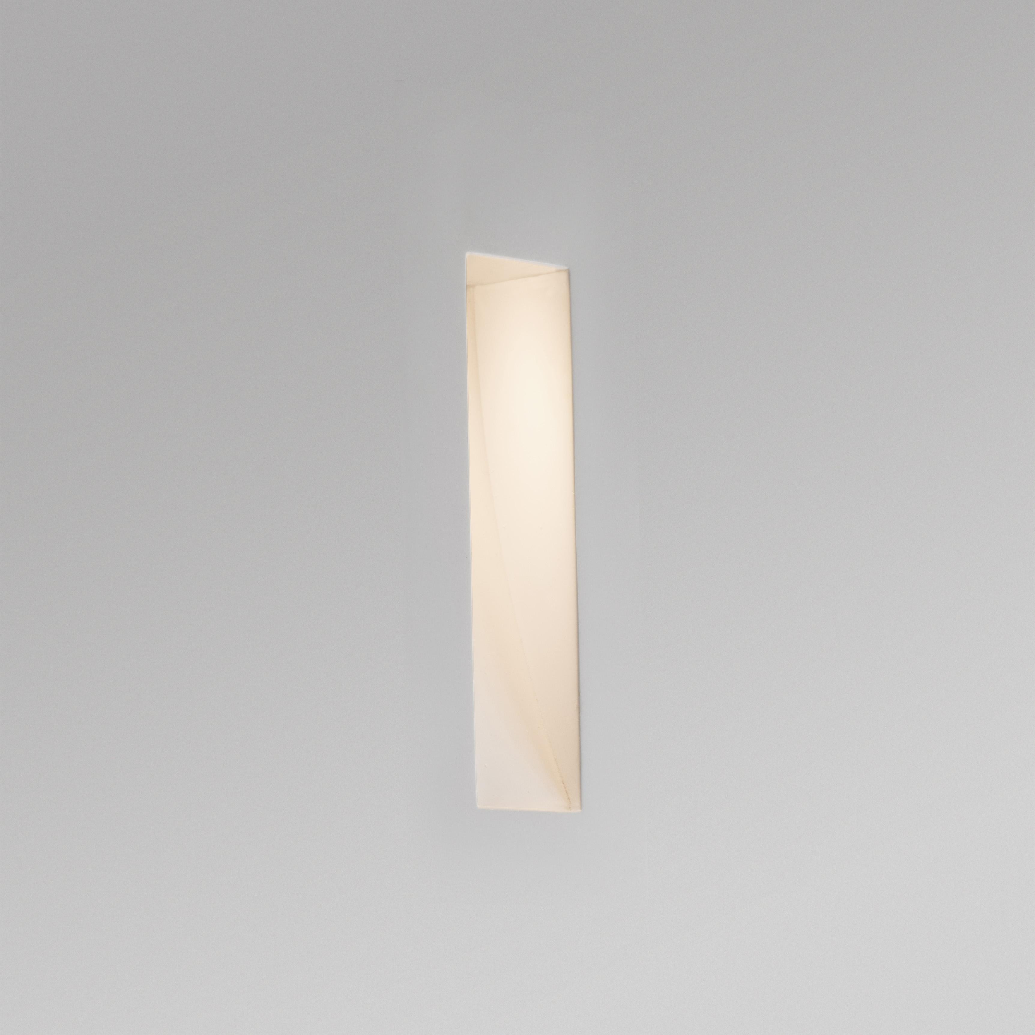 Una lampada da parete verticale lunga e sottile su una parete grigia. La luce è accesa.