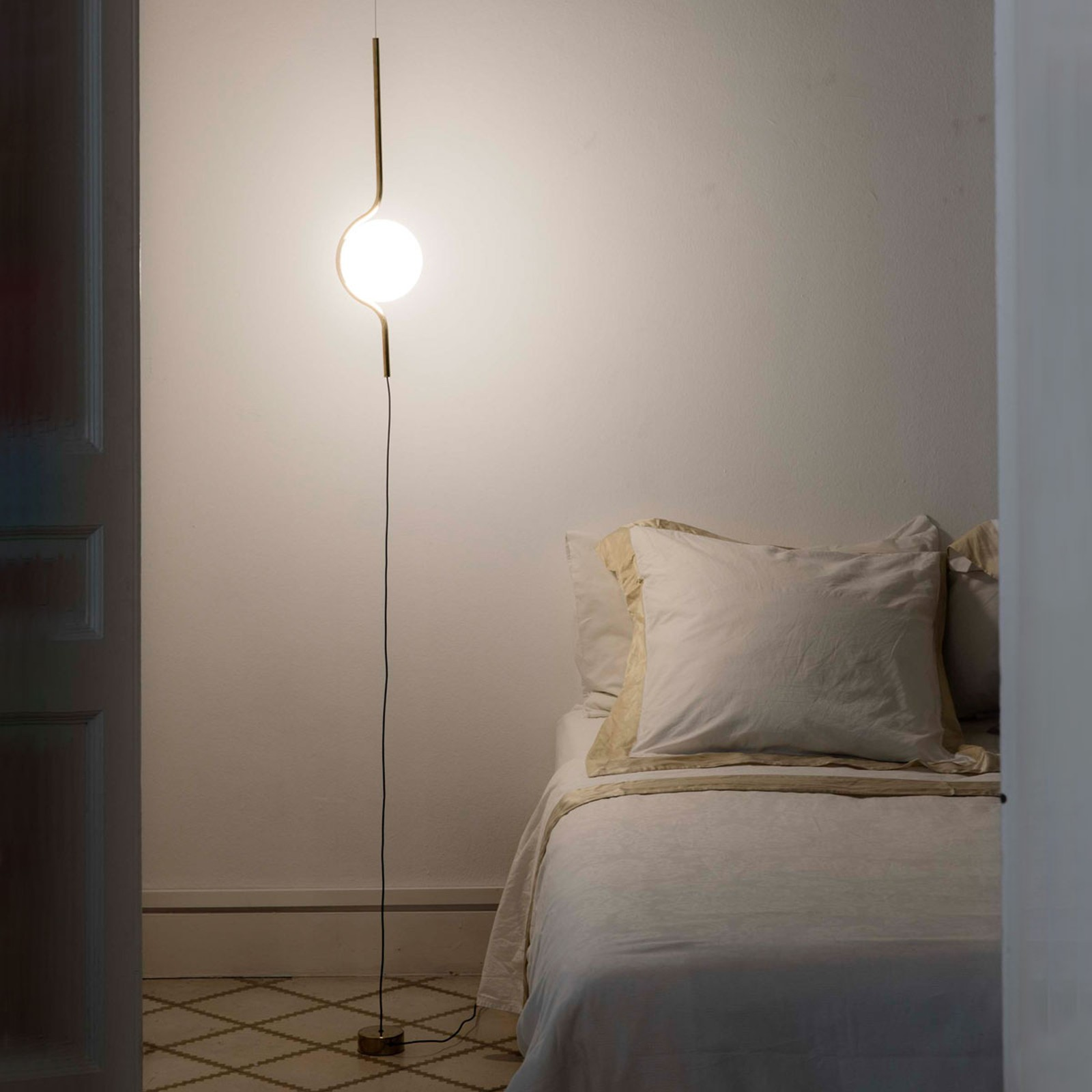 Una lampada da terra moderna con un globo bianco e una cornice sottile, accanto a un letto.