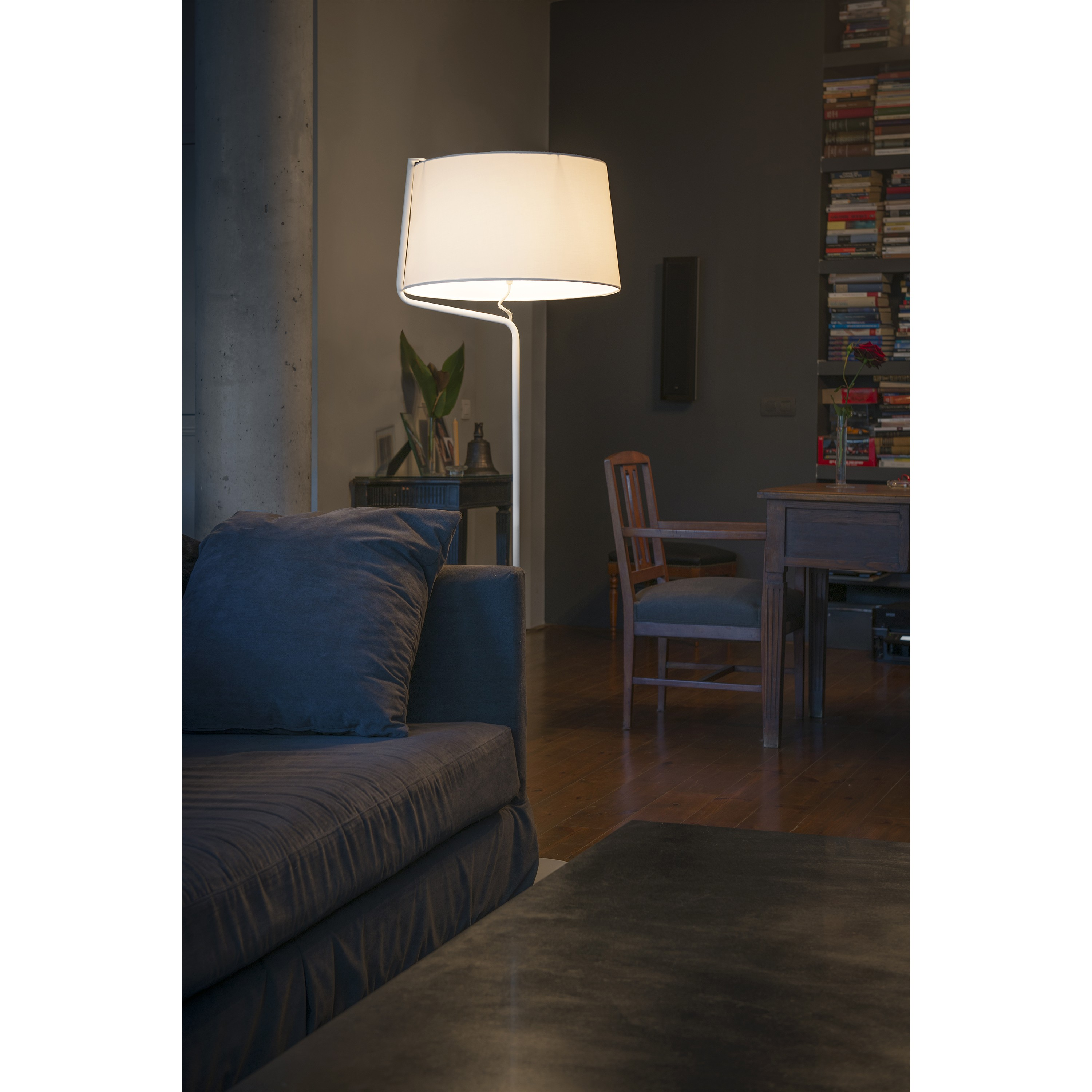 Soggiorno con una lampada da terra. C'è un divano, un tavolo e una libreria sullo sfondo.