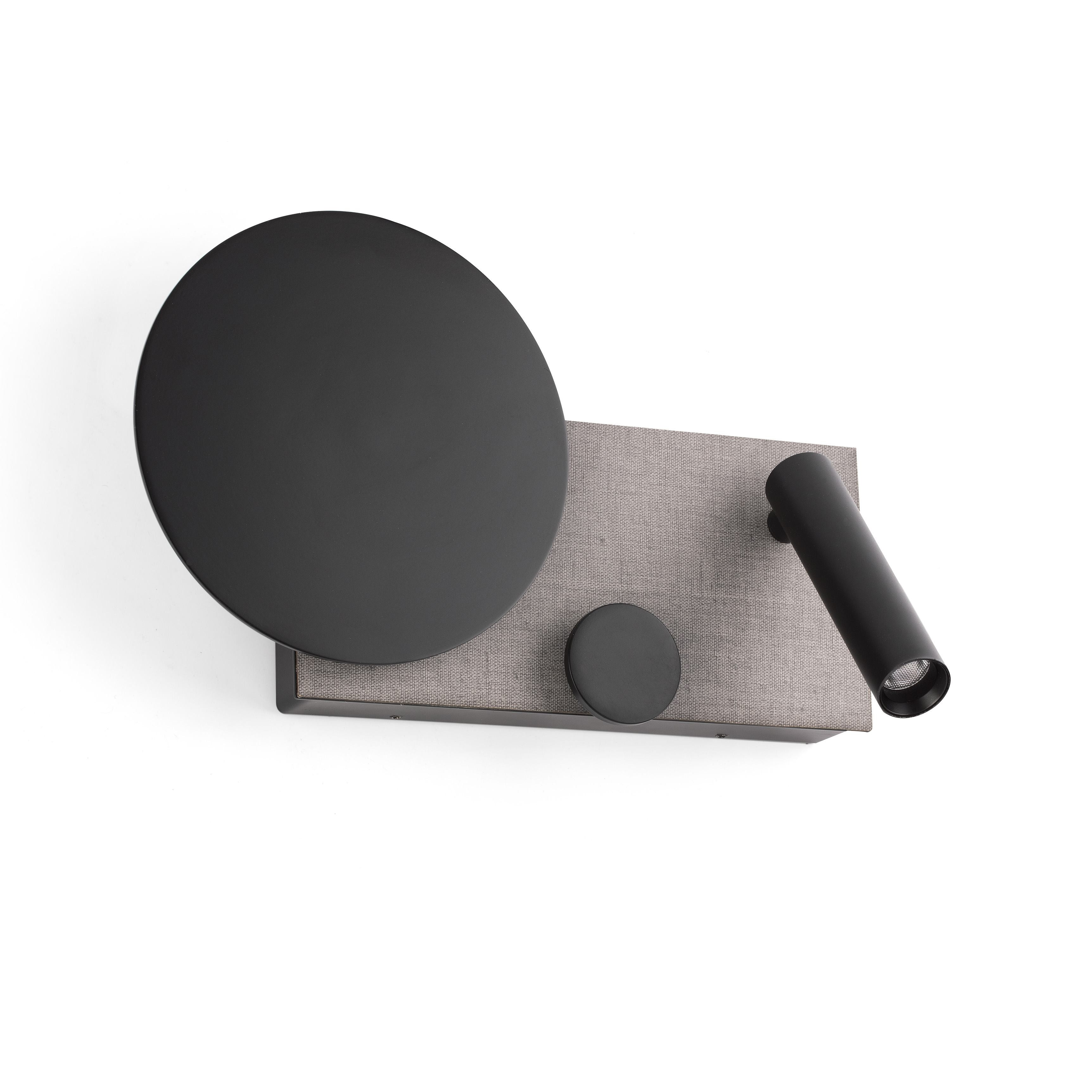 Lampada da parete con un disco nero e una luce a cilindro. Il tessuto grigio fa parte del design.