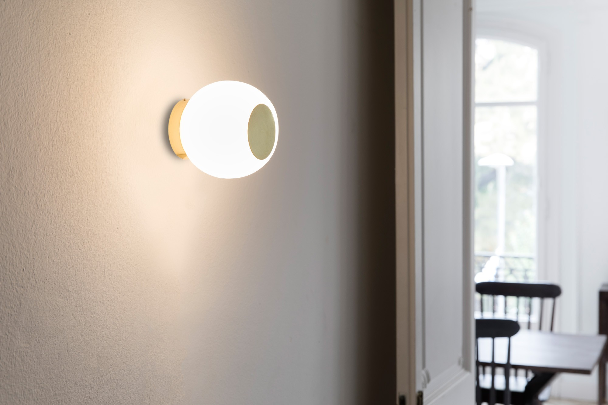 Lampada da parete con sfera bianca e accento dorato. La luce è accesa, illuminando il muro.