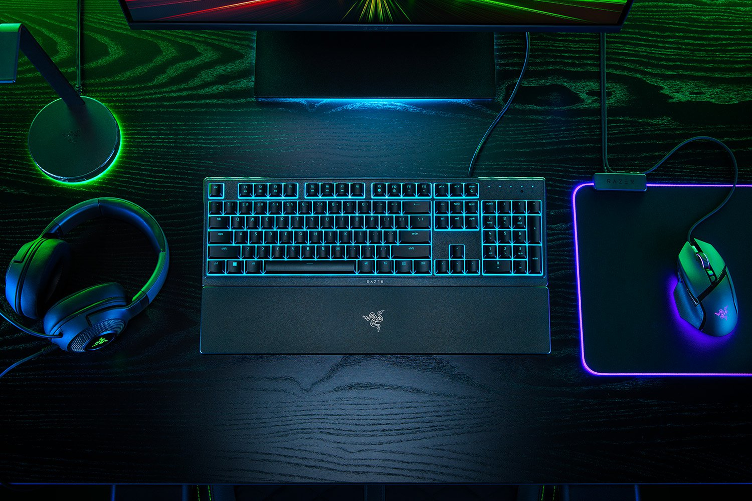 Configurazione di gioco: tastiera, mouse, cuffie e monitor su una scrivania scura. Marchio Razer.