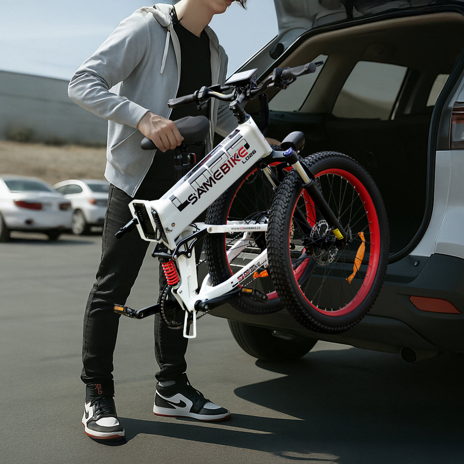 Osoba ładująca biały składany rower elektryczny z czerwonymi obręczami do bagażnika samochodu.