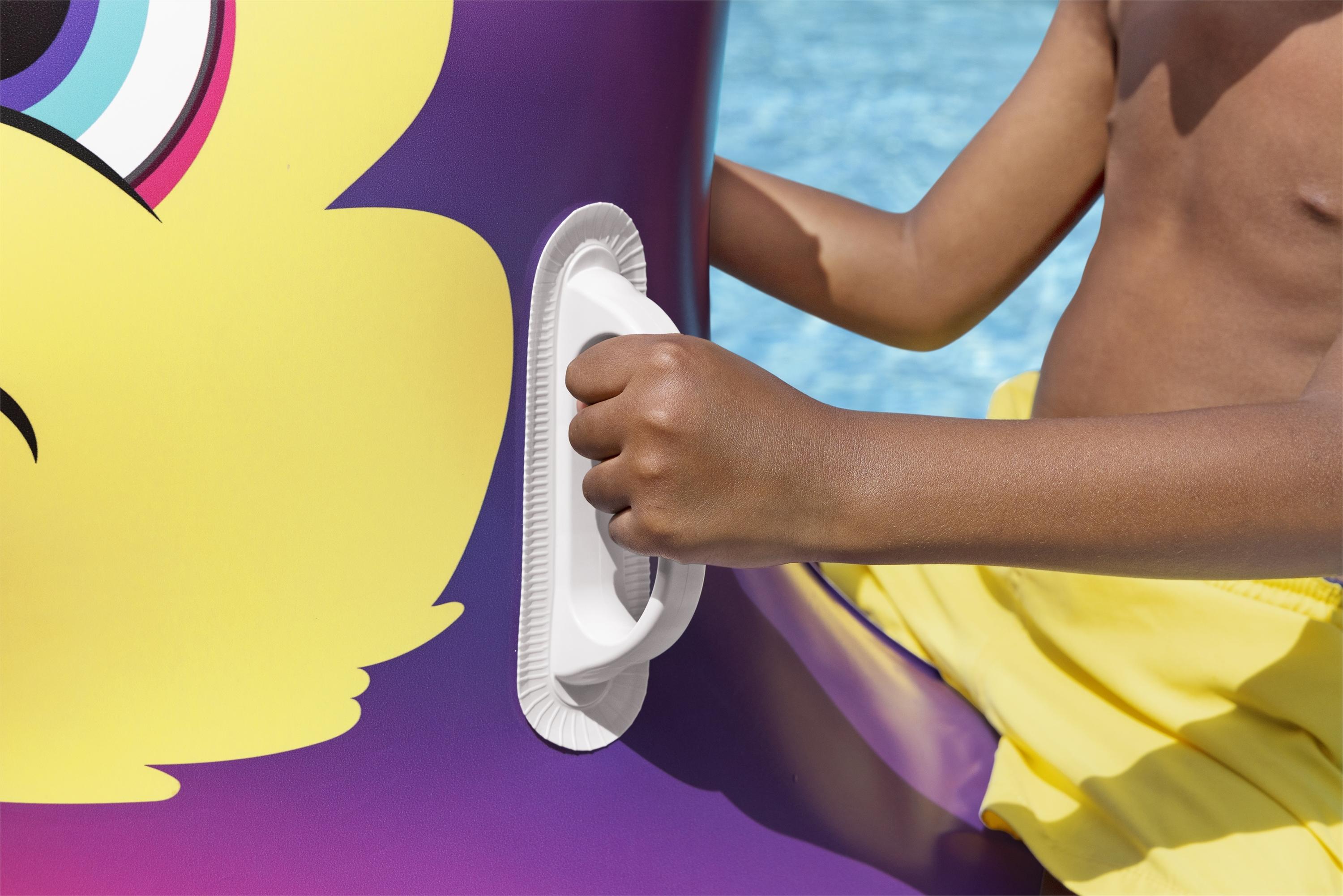 Dłoń dziecka trzymająca biały uchwyt na fioletowym i żółtym nadmuchiwanym pływaku.