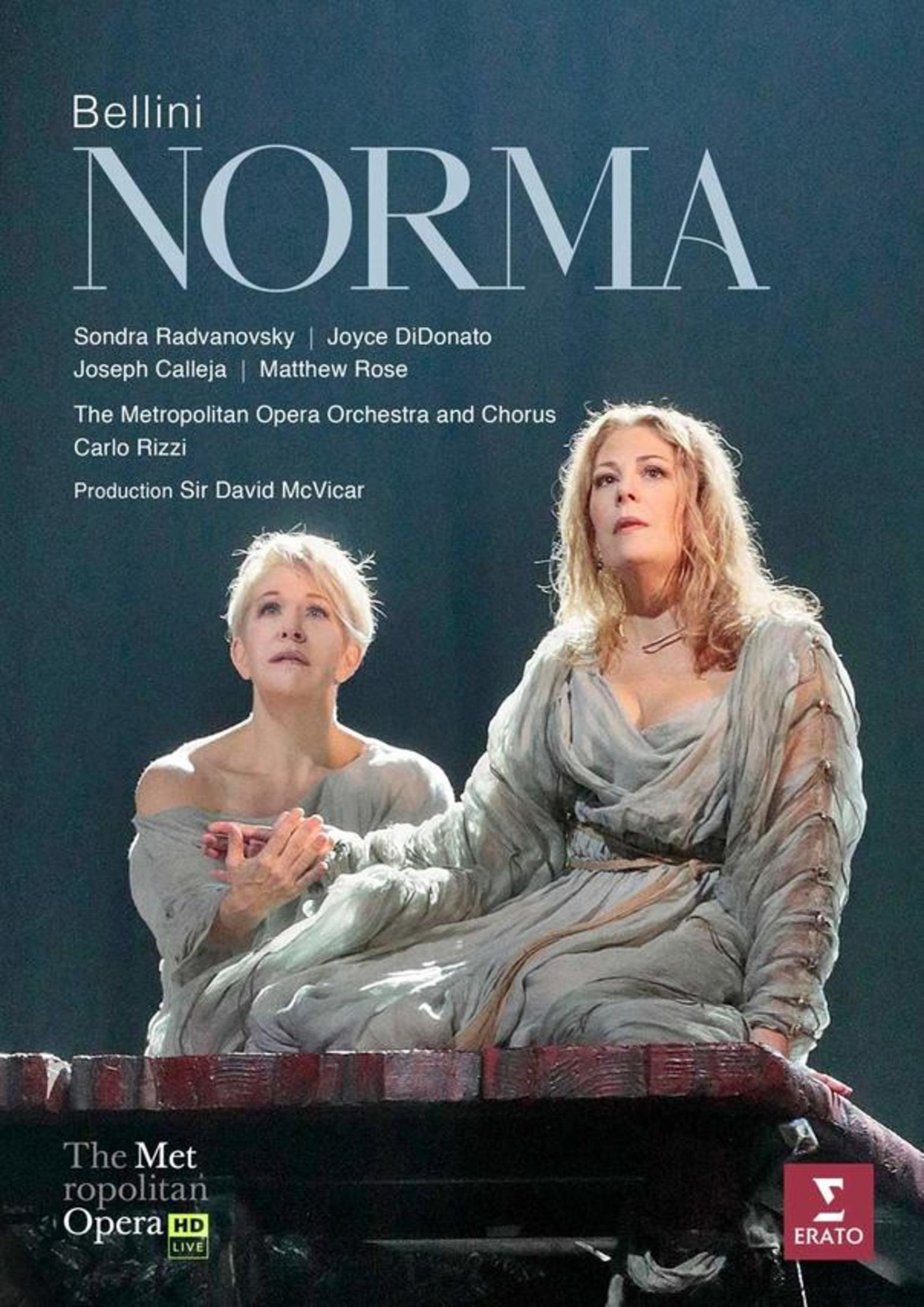 Plakat operowy. Dwie kobiety w szarych sukniach na scenie. Tekst: 'Norma' Belliniego. Logo Met Opera.