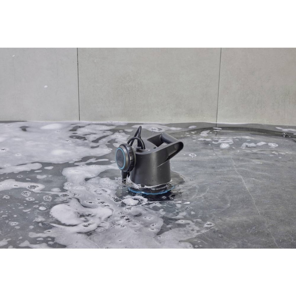 Czarne urządzenie czyszczące zanurzone w mydlanej wodzie na szarej kafelkowej powierzchni.