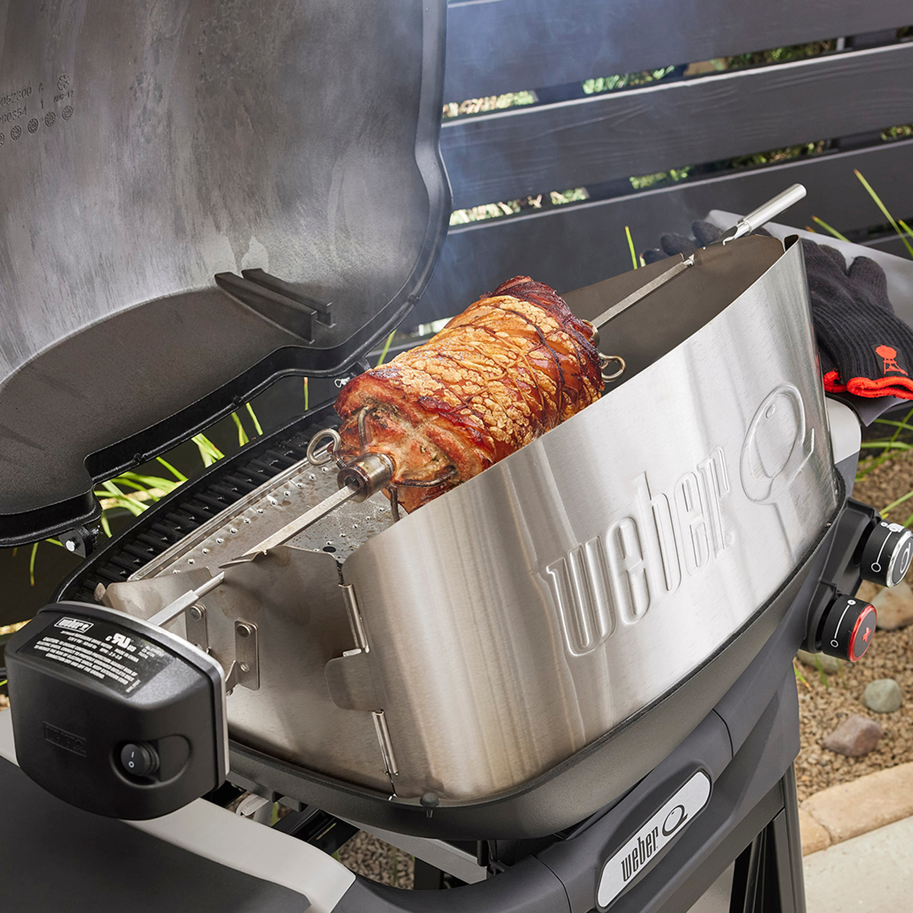 Parrilla Weber con un lomo de cerdo asado en un asador. La parrilla está abierta y el interior es visible.