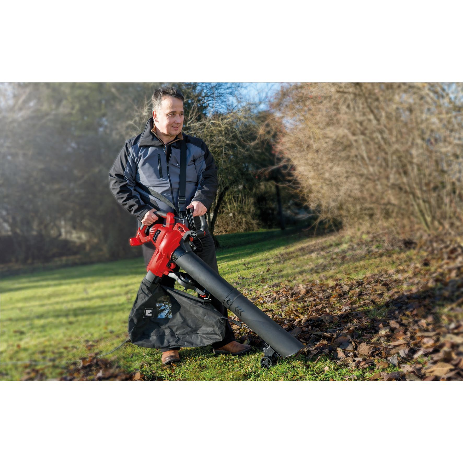 Man using a leaf blower on a grassy area with leaves.