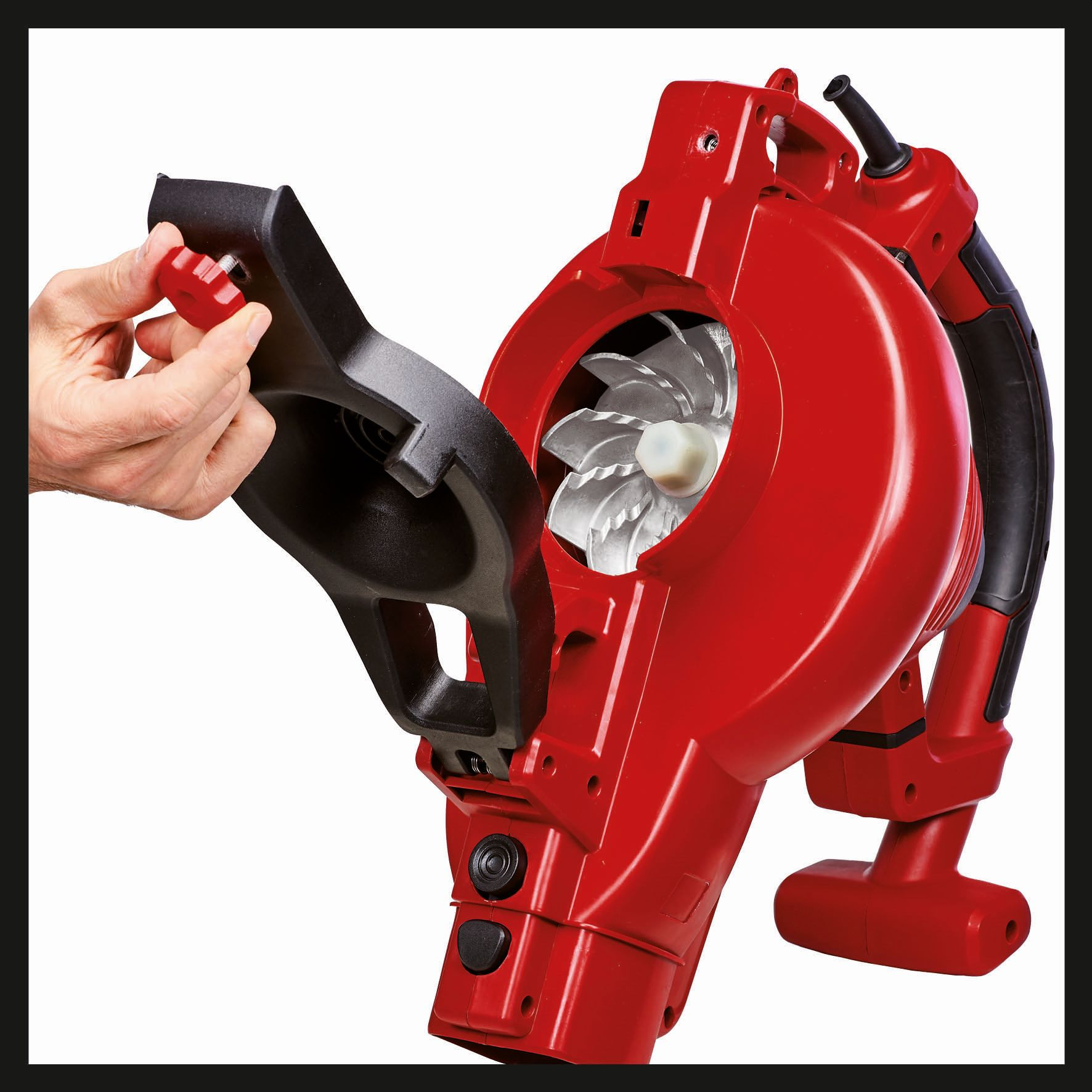 A red leaf blower with a person's hand adjusting a part.