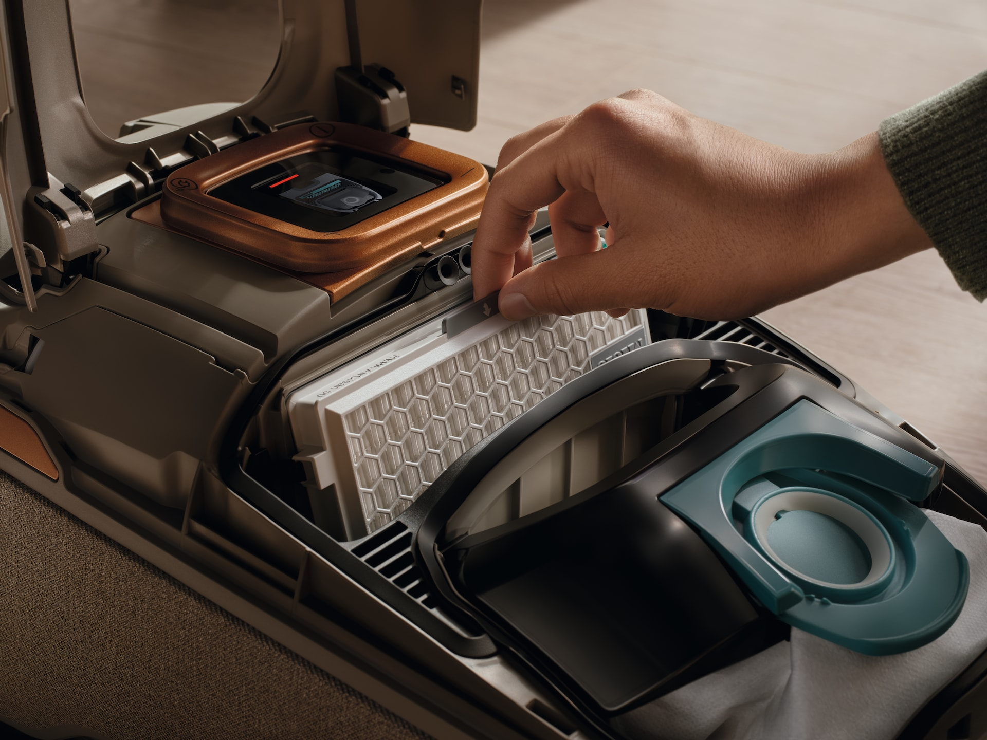 Dłoń wkładająca biały filtr powietrza do odkurzacza. Odkurzacz jest otwarty.