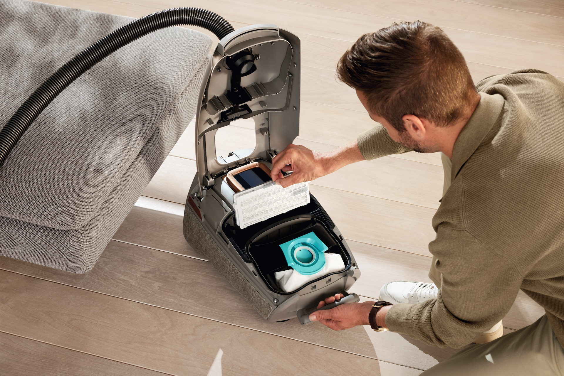 Osoba wymienia filtr w odkurzaczu. Obok nich jest sofa.