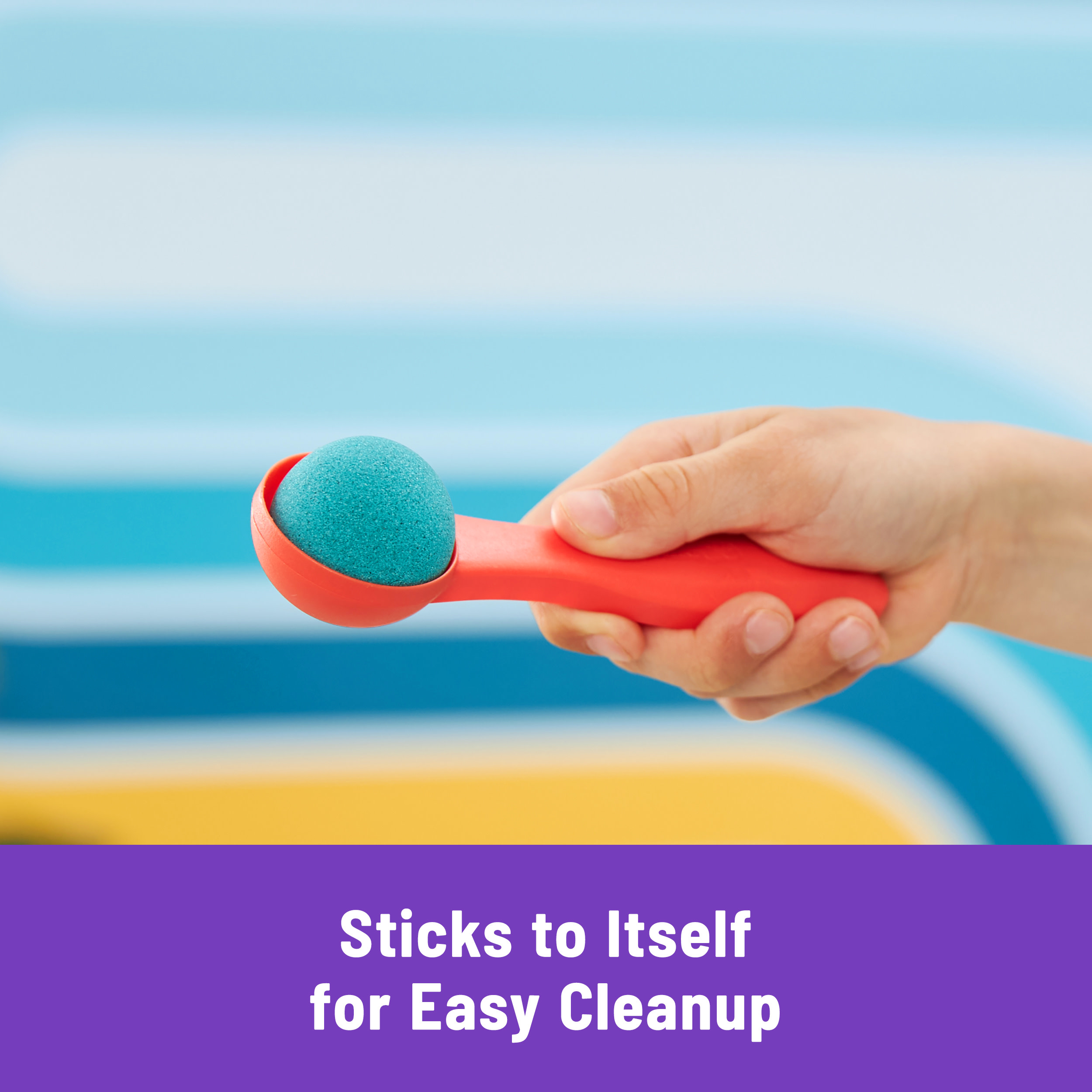 Ręka trzymająca pomarańczową łyżkę z niebieską kulką piasku. Tło to kolorowy, rozmyty wzór.