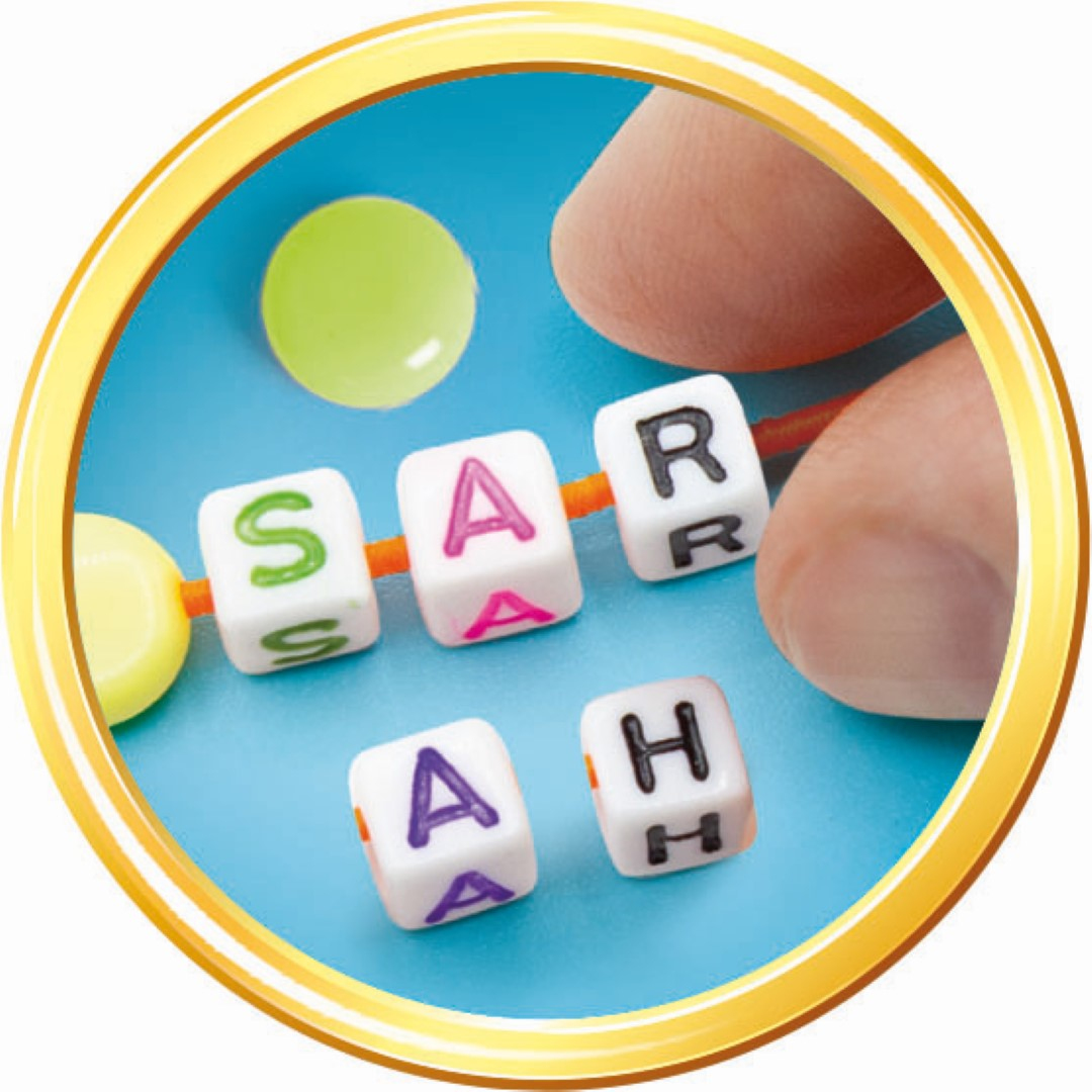 Zbliżenie dłoni nawlekającej koraliki, aby przeliterować 'SARAH'. Koraliki są białe z literami i kolorowymi akcentami.