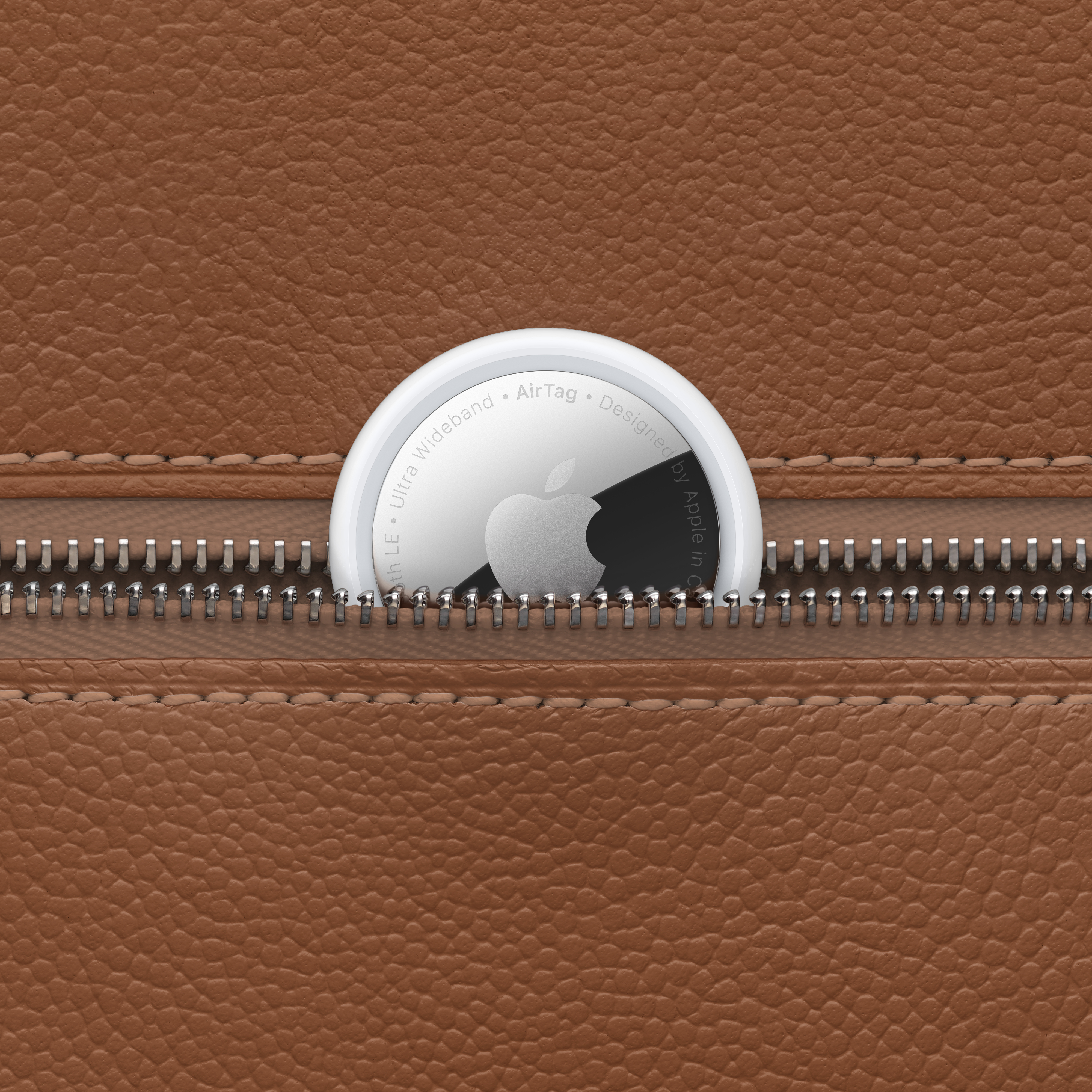 Beyaz bir Apple AirTag, kahverengi deri bir cebin içinde kısmen fermuarlı.