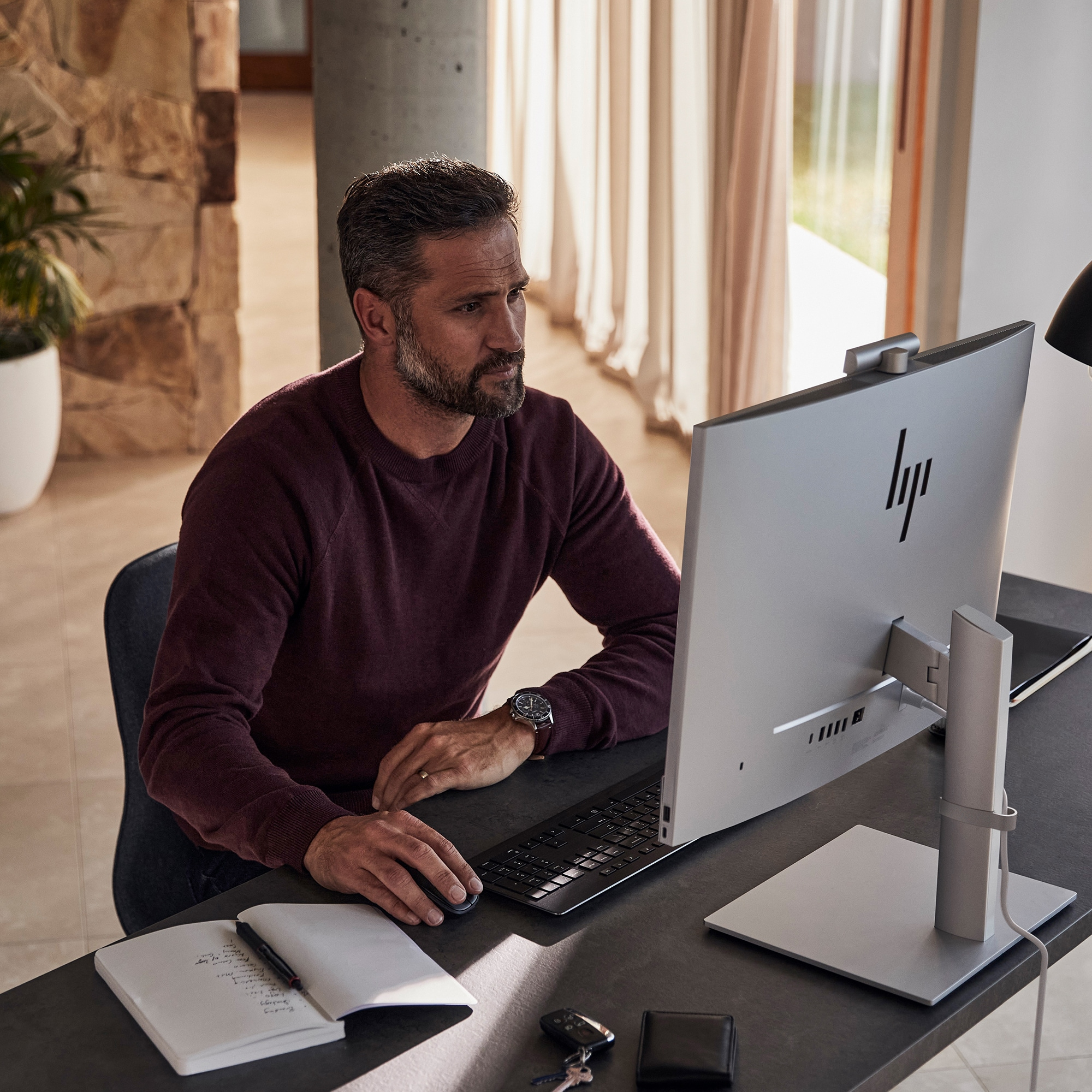 Uomo che usa un computer con un monitor HP. È seduto a una scrivania con una tastiera.