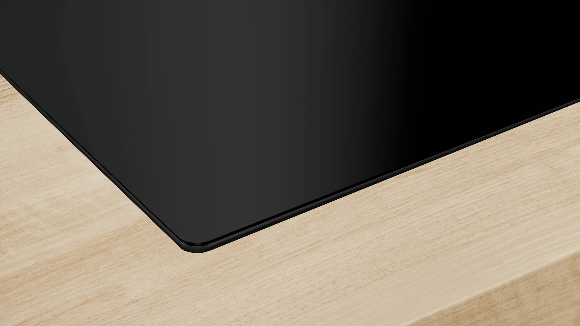 Un primo piano di un piano cottura nero con bordo in legno chiaro.