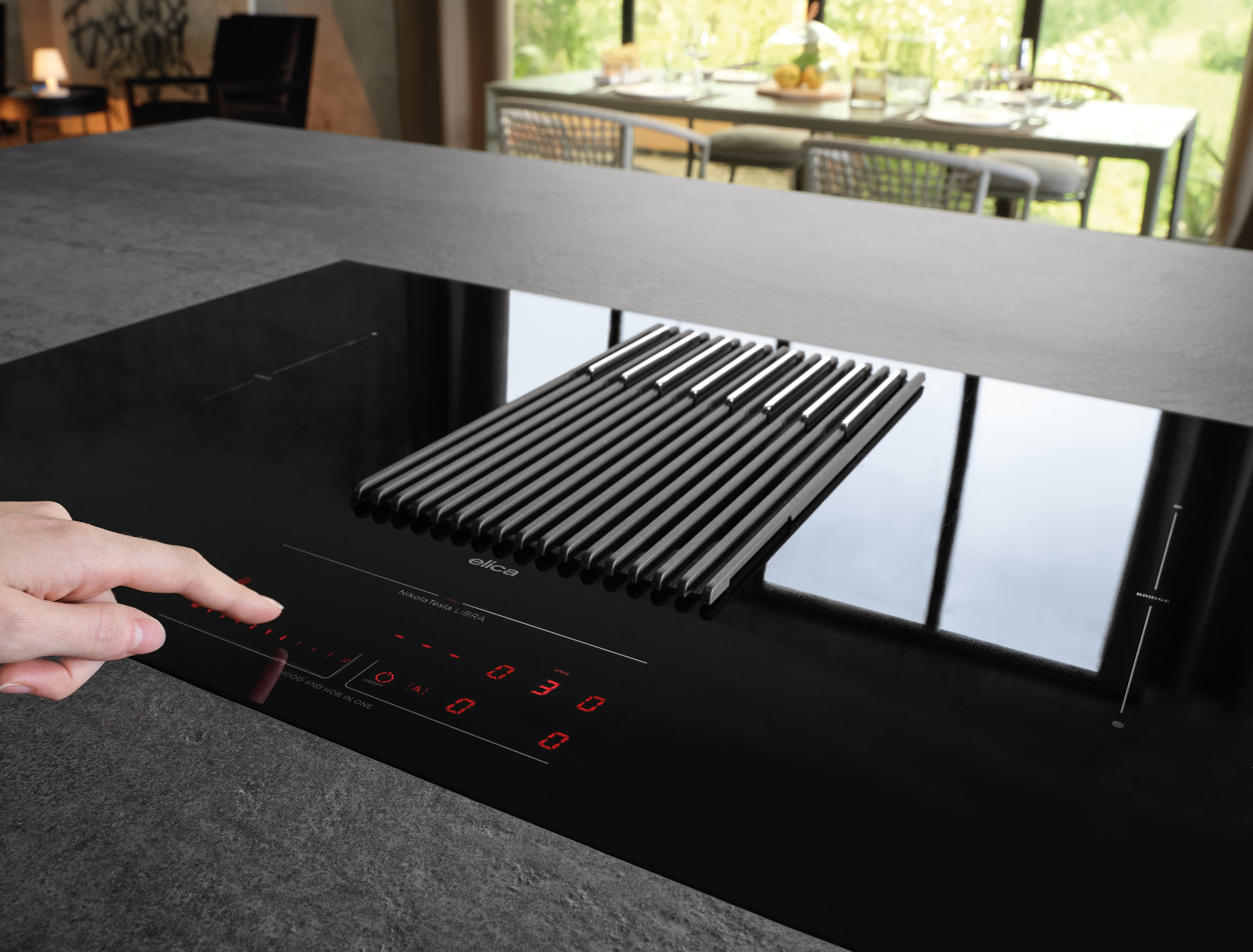Un piano cottura a induzione nero con aspiratore integrato e un dito che tocca i comandi.