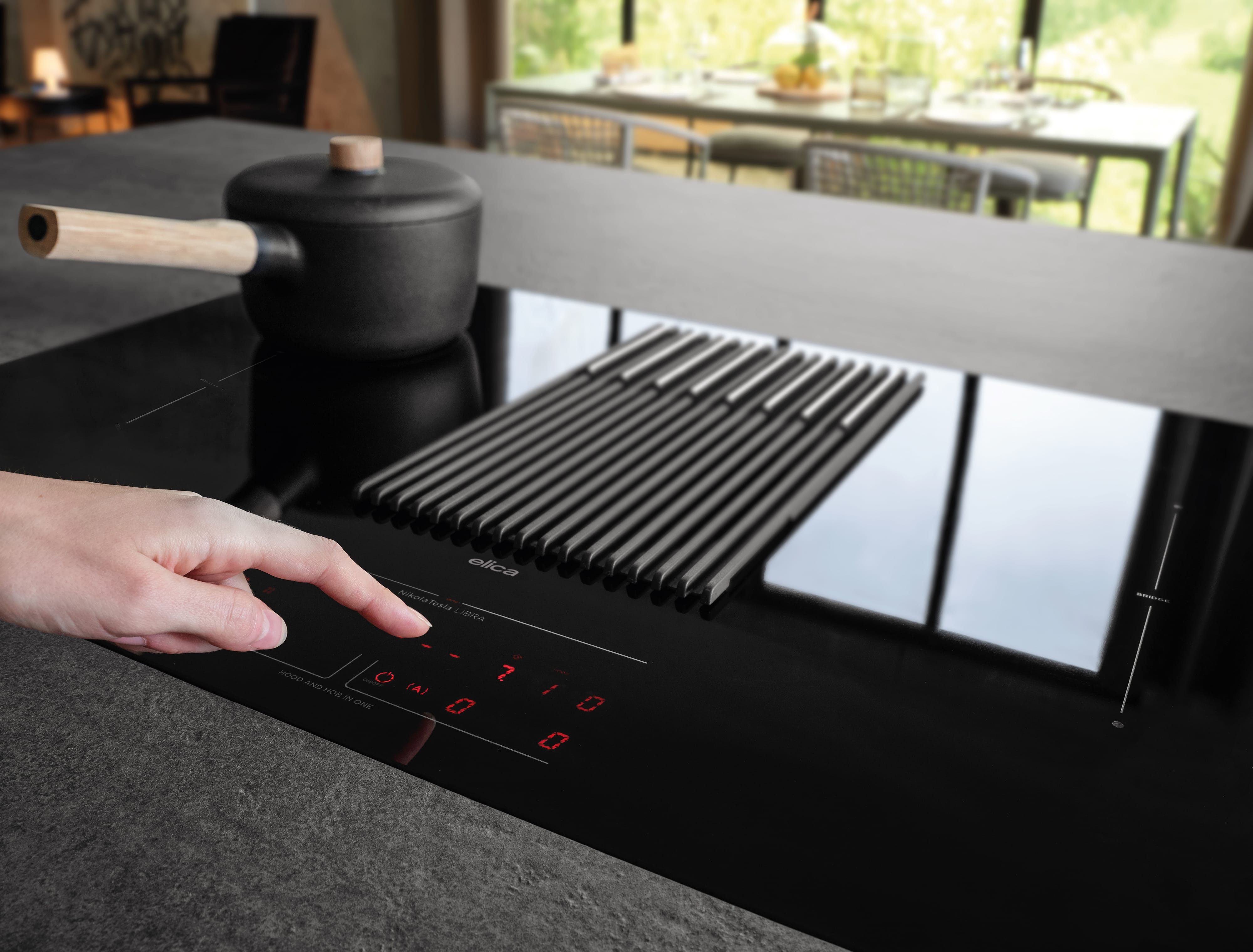 Un dito che preme un pulsante su un piano cottura nero con una pentola e una griglia sopra.