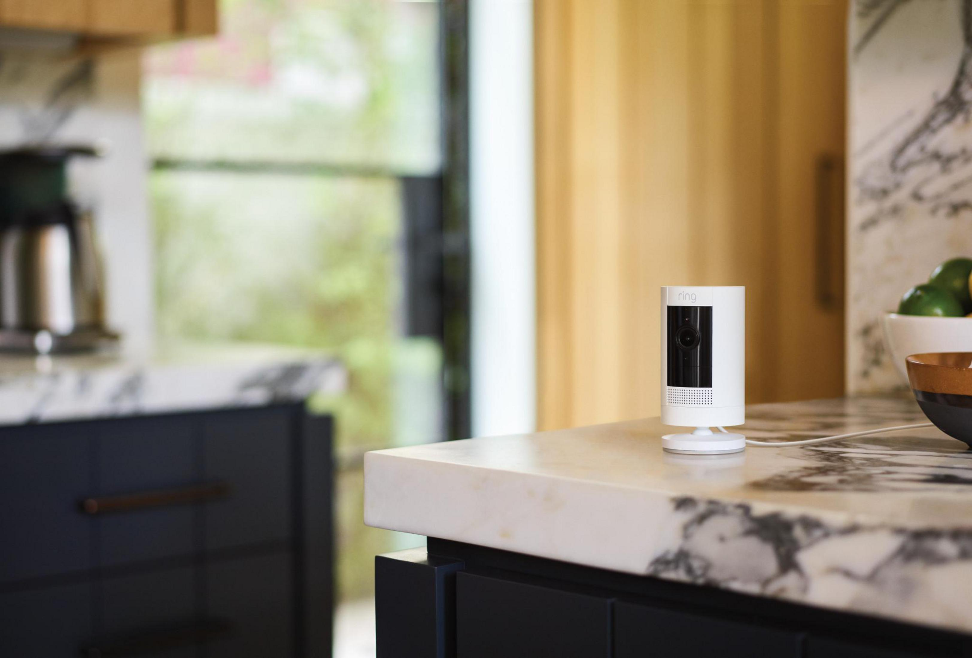 White security camera on a white counter in a kitchen. The background is blurred.